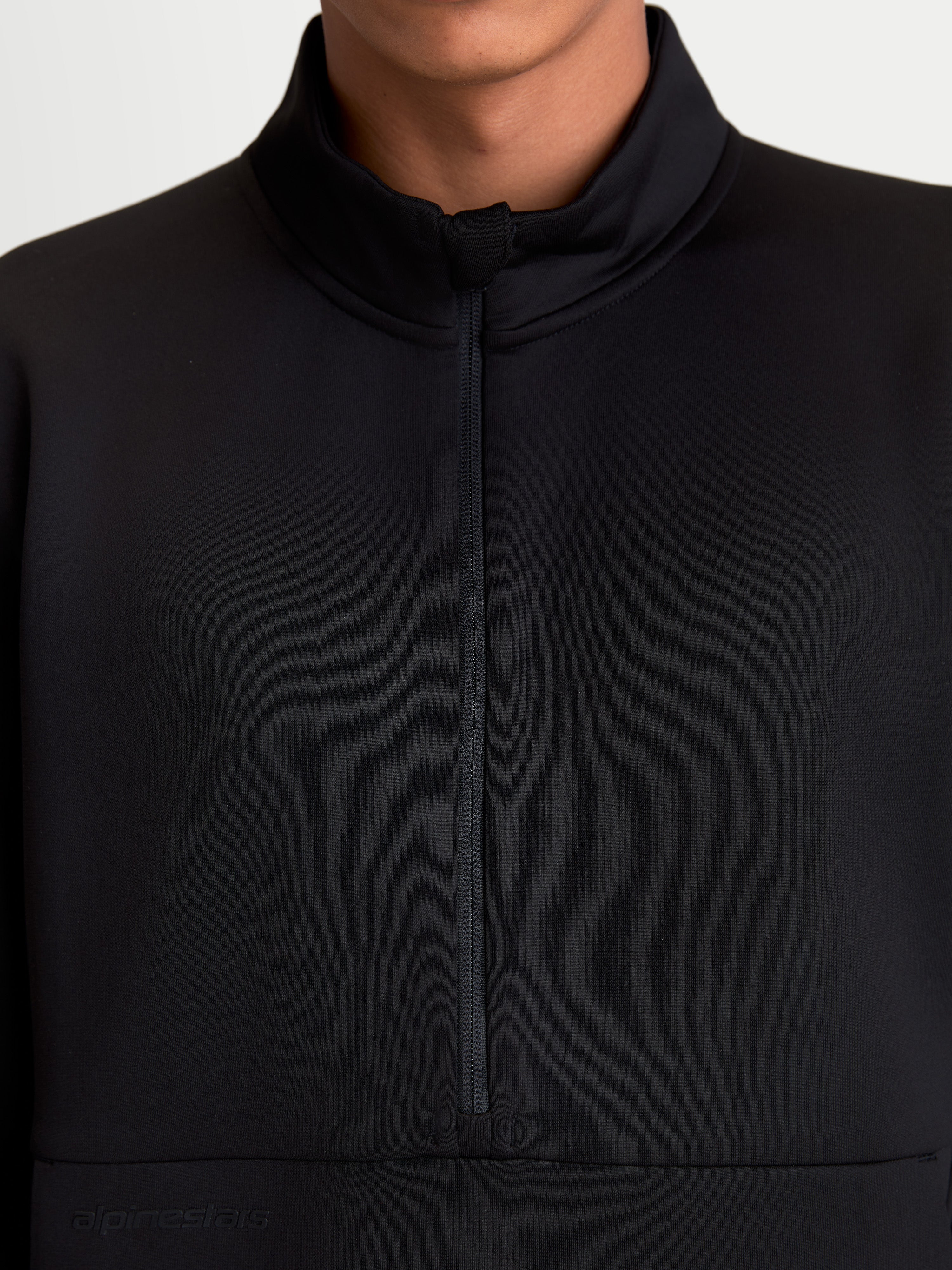 Alpinestars Felpa Apera Half-Zip, dettaglio in primo piano della chiusura a mezza zip e del colletto alto, indossata, nera, in pile tri-blend con logo tonale Alpinestars, stile sportswear ispirato al motorsport