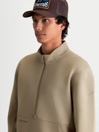 Alpinestars Felpa Apera Half-Zip, pullover sportswear da uomo, beige, con chiusura a mezza zip, tasca a marsupio e branding tonale, abbigliamento casual motorsport indossato da un modello.