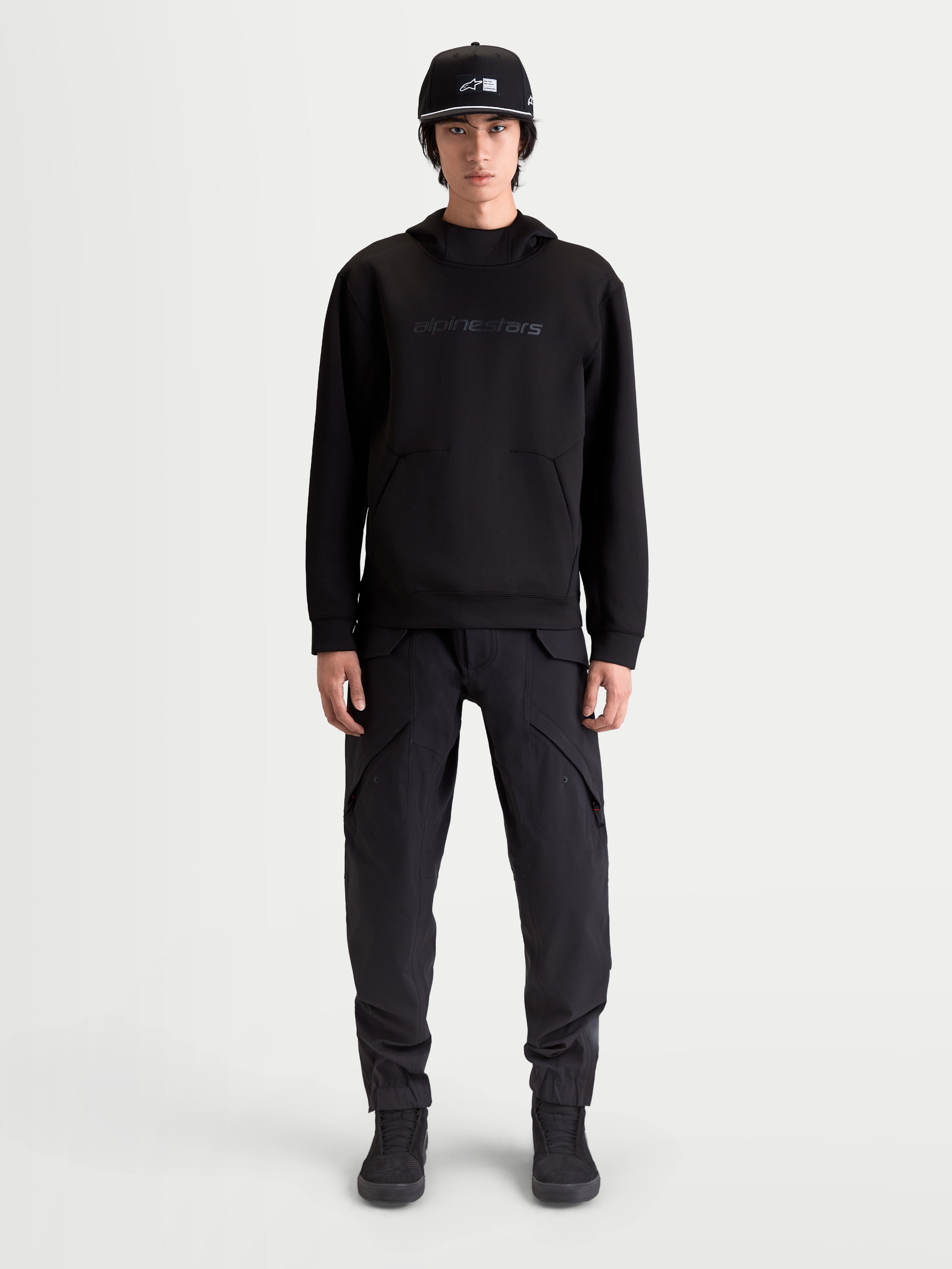 Alpinestars felpa con cappuccio Datrix, pullover sportswear premium da uomo, nera, branding Alpinestars HD tono su tono, pile tri-blend double-face e tasca con dettaglio a freccia, indossata da un modello per uno stile ispirato al motorsport