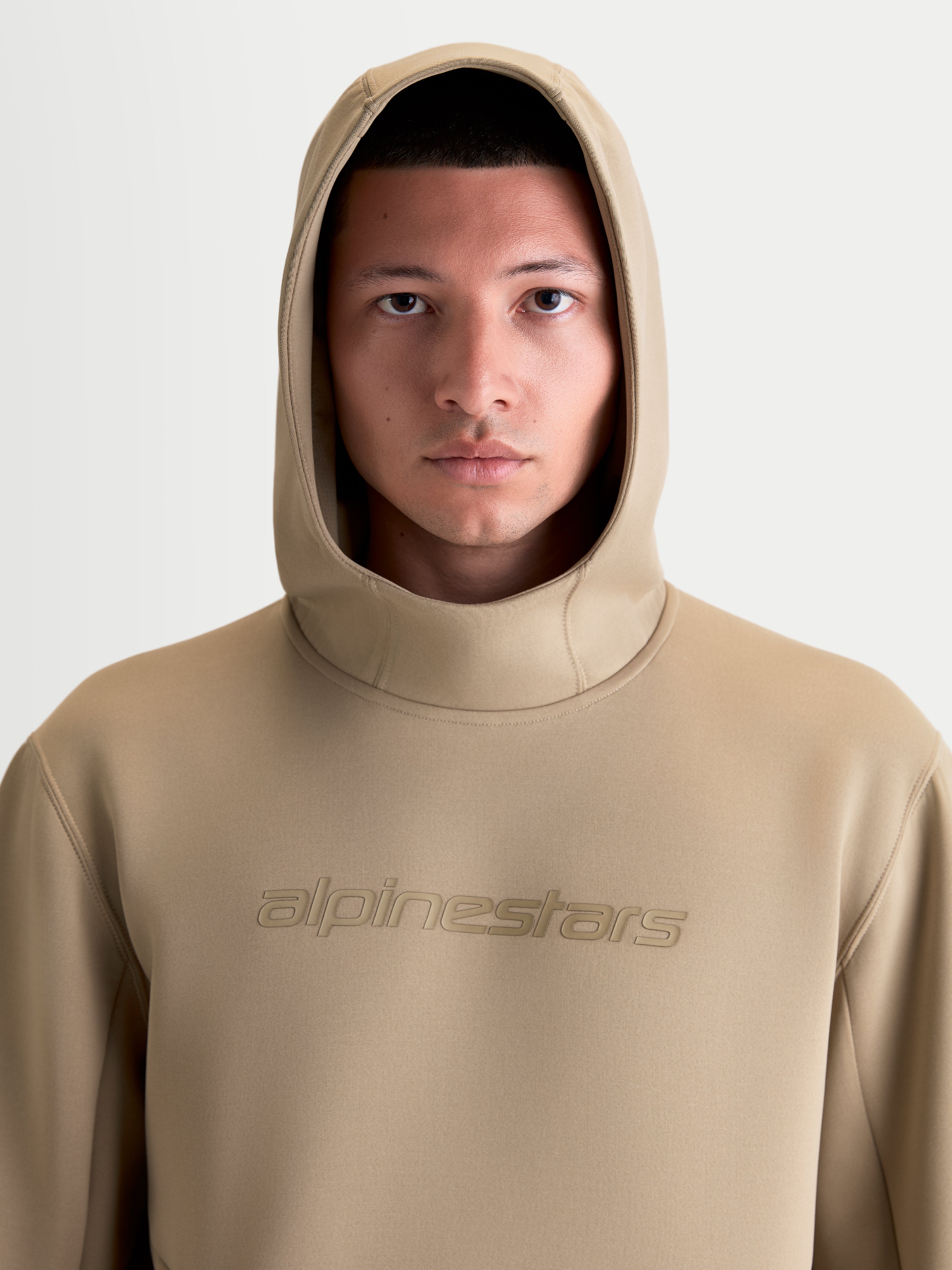 Alpinestars Felpa con cappuccio Datrix, felpa sportswear premium unisex, marrone, primo piano frontale su modello con cappuccio alzato, branding Alpinestars HD tono su tono, materiale in pile tri-blend di alta qualità.