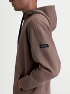 Alpinestars Felpa con cappuccio Camino Textured Oversized, pullover sportswear casual, marrone, vista laterale su modello con pile in twill testurizzato ed etichetta logo Alpinestars sulla manica