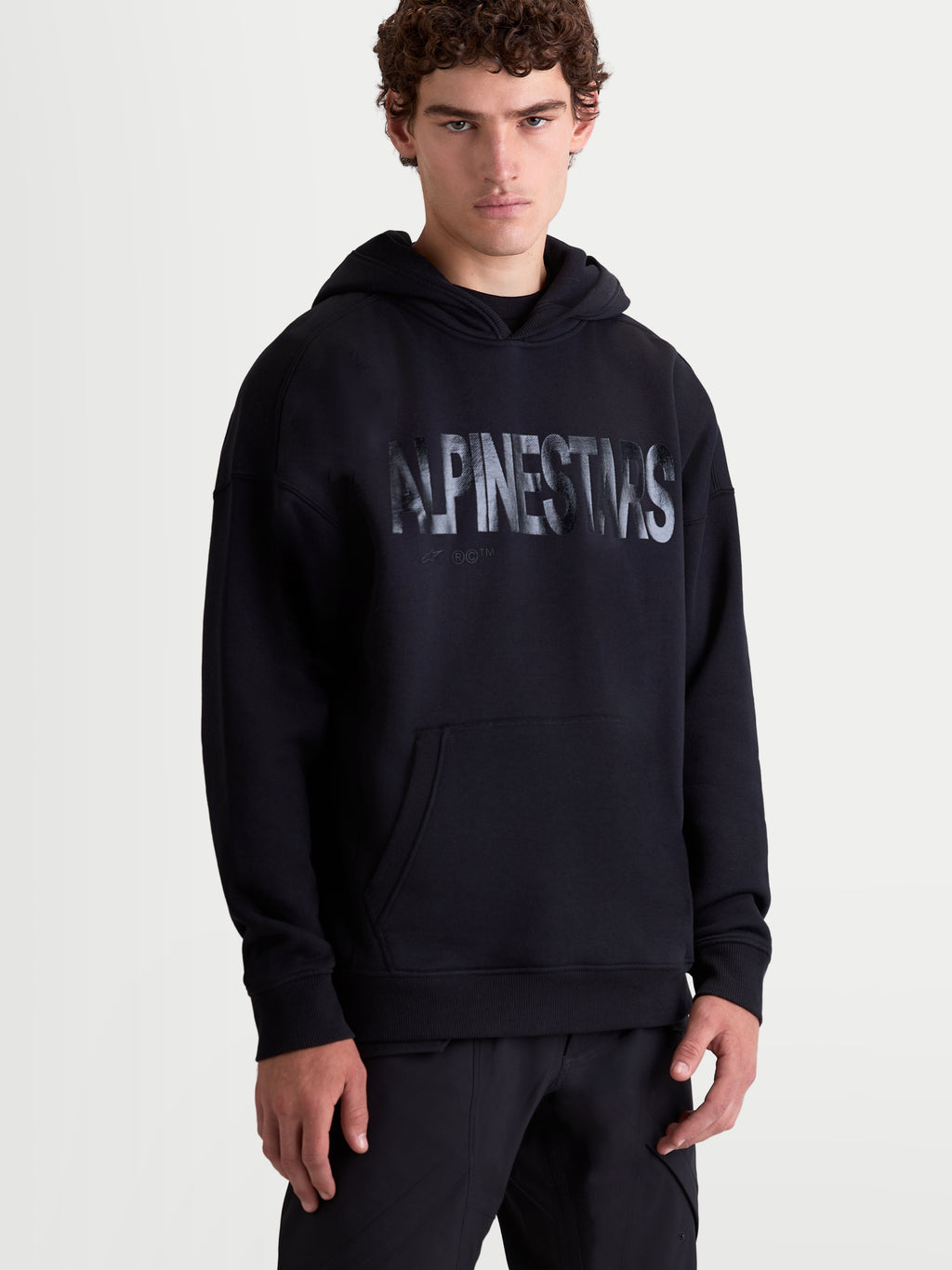 Alpinestars Felpa con cappuccio Shaw Oversize, felpa sportswear da uomo con vestibilità rilassata, nera, logo Alpinestars testurizzato sul petto, tasca a marsupio e cappuccio foderato, in pile di cotone e poliestere riciclato, vista frontale su modello.