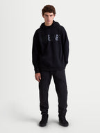Alpinestars Felpa con cappuccio Shaw oversize, felpa casual sportswear da uomo, nera, vestibilità rilassata in pile con logo Alpinestars testurizzato sul petto, tasca a marsupio e cappuccio foderato, vista frontale su modello