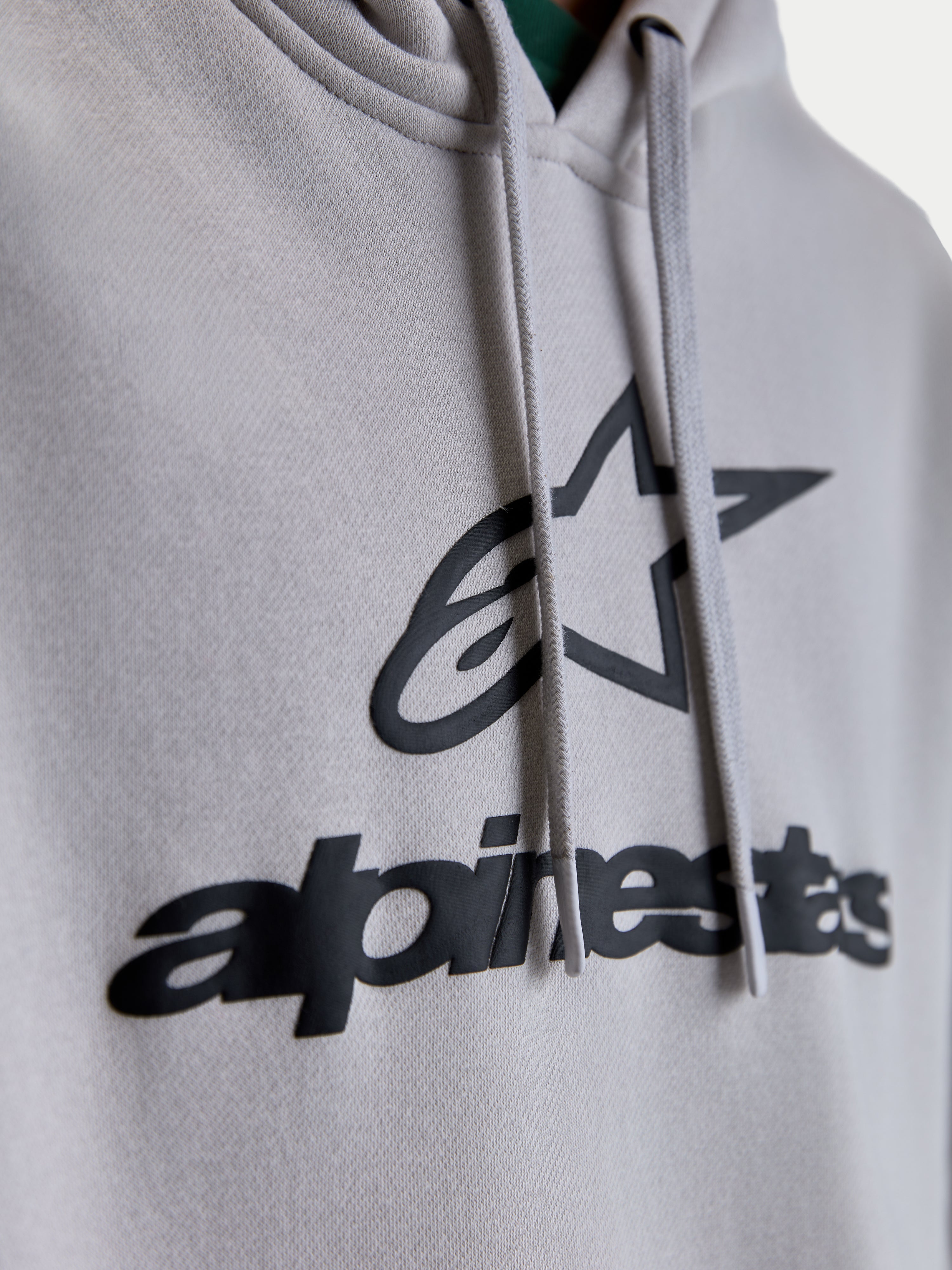 Alpinestars Felpa con cappuccio Prelude Oversized, dettaglio del logo con stampa a rilievo e grafica a stella neri su pile grigio cemento, cordini piatti, sportswear premium unisex