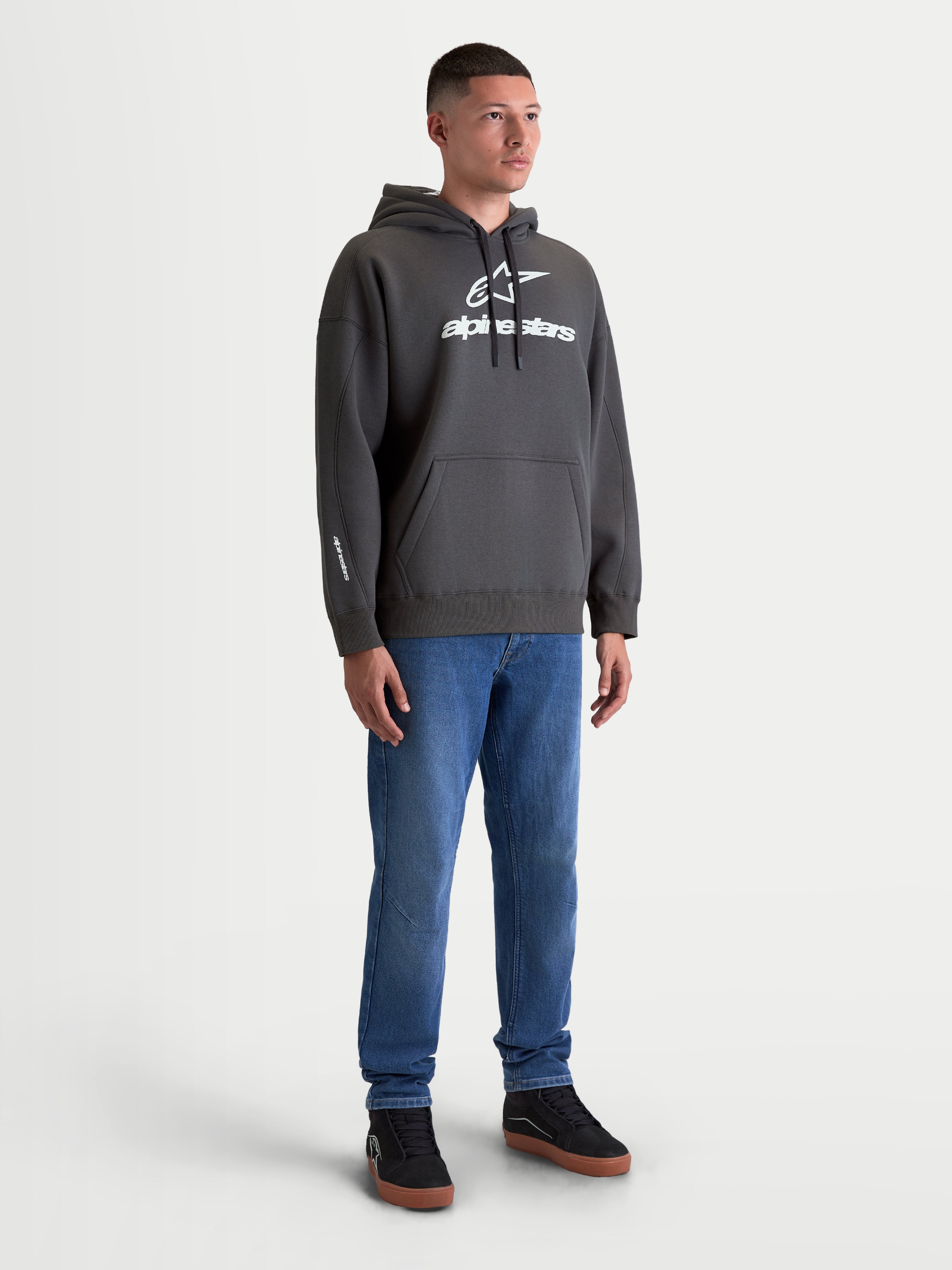Alpinestars felpa con cappuccio Prelude Oversized, felpa sportswear in pile grigio antracite con logo bianco a rilievo sul petto, vestibilità oversize, tasca a marsupio e cappuccio foderato, look casual lifestyle indossato da un modello.