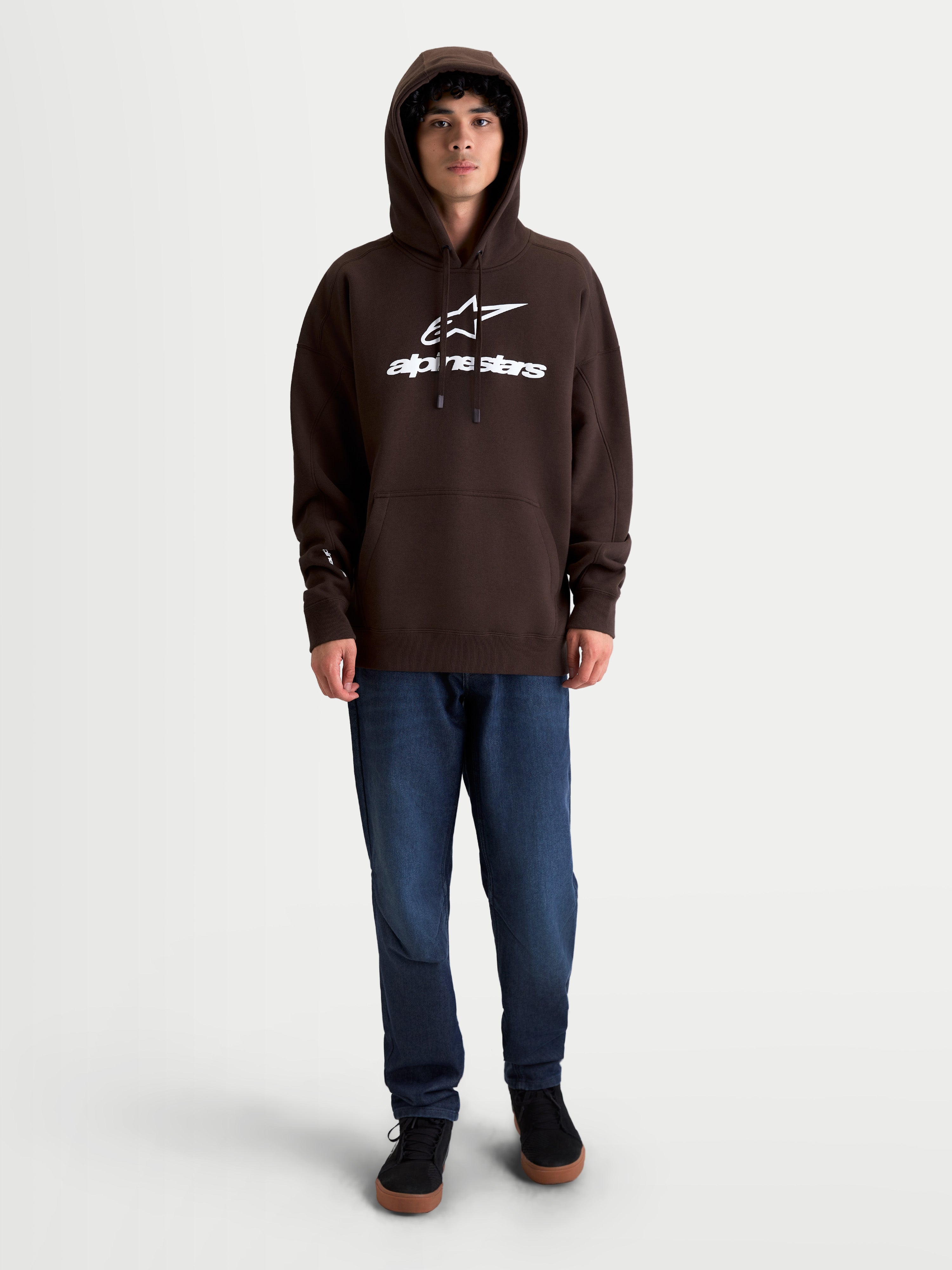 Alpinestars Felpa con cappuccio Prelude Oversized, felpa sportswear unisex in pile, marrone, logo bianco a rilievo sul petto, vestibilità rilassata, tasca a marsupio e cappuccio foderato, indossata da un modello