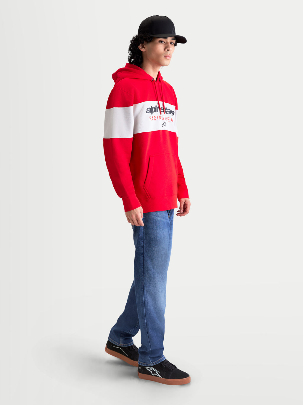 Alpinestars Felpa con cappuccio Cubic, felpa sportswear da uomo in pile rossa e bianca, con design a blocchi di colore e logo Alpinestars sul petto. Vista laterale su modello che mostra il cappuccio, la tasca a marsupio e i polsini a coste, ideale per un look casual fuori dalla moto.