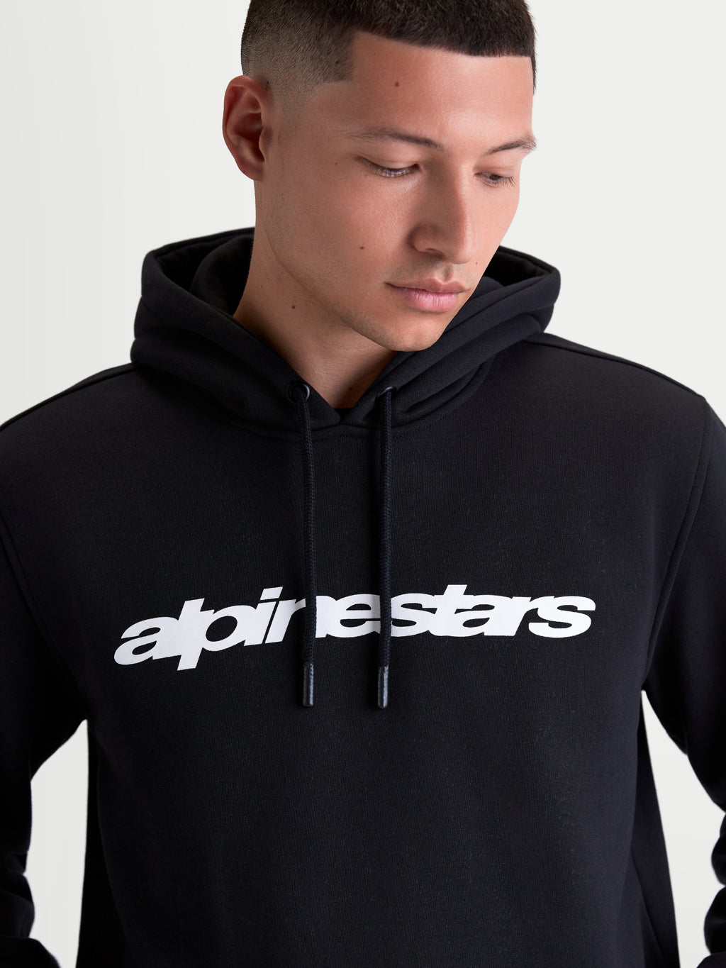 Alpinestars felpa con cappuccio Race Wordmark, felpa sportswear in pile nero indossata da un modello, con logo wordmark bianco sul petto, cappuccio autofoderato e terminali del cordino immersi, stile motorsport casual, realizzata in cotone e poliestere riciclato.