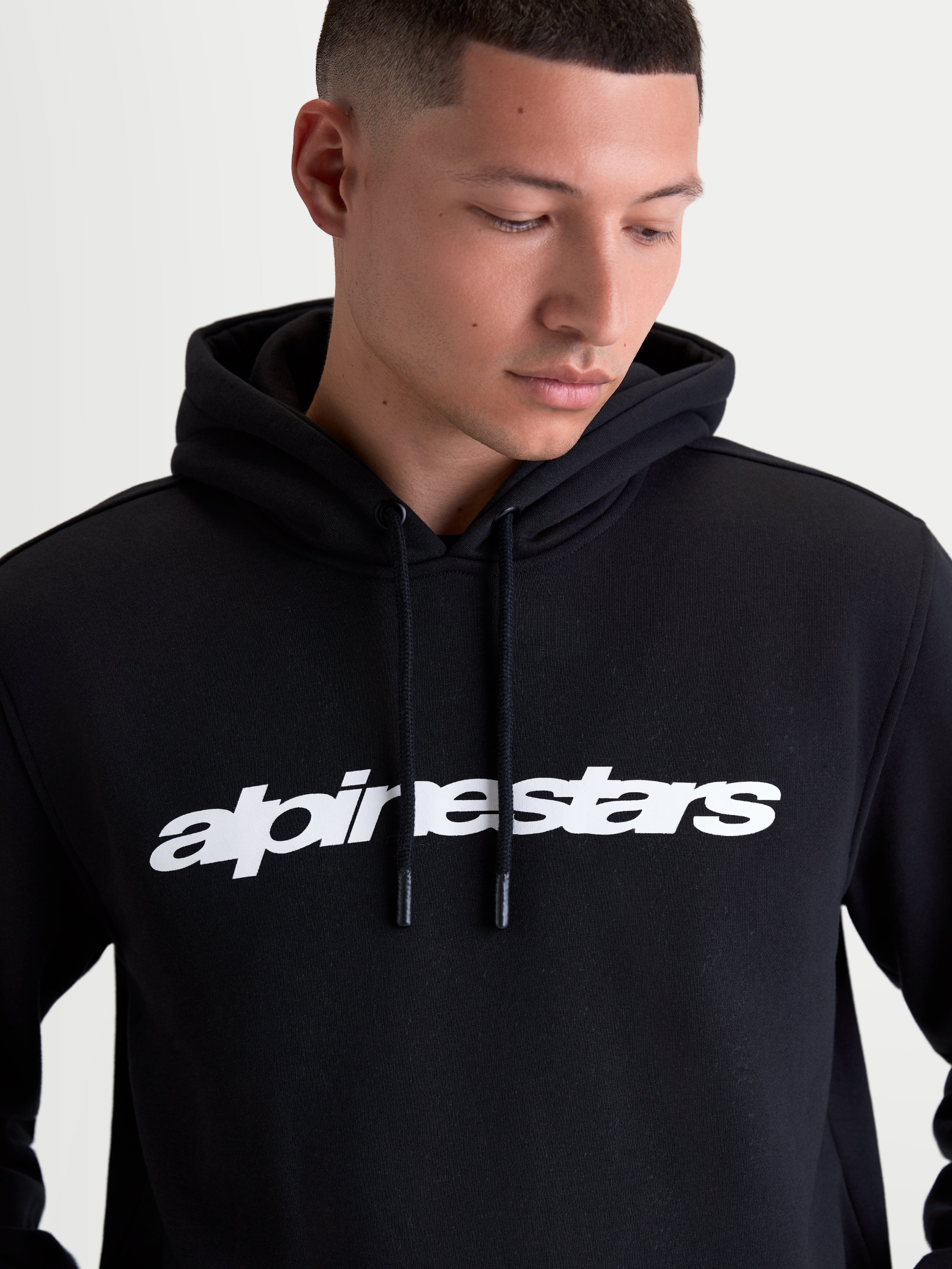 Alpinestars felpa con cappuccio Race Wordmark, felpa sportswear in pile nero indossata da un modello, con logo wordmark bianco sul petto, cappuccio autofoderato e terminali del cordino immersi, stile motorsport casual, realizzata in cotone e poliestere riciclato.