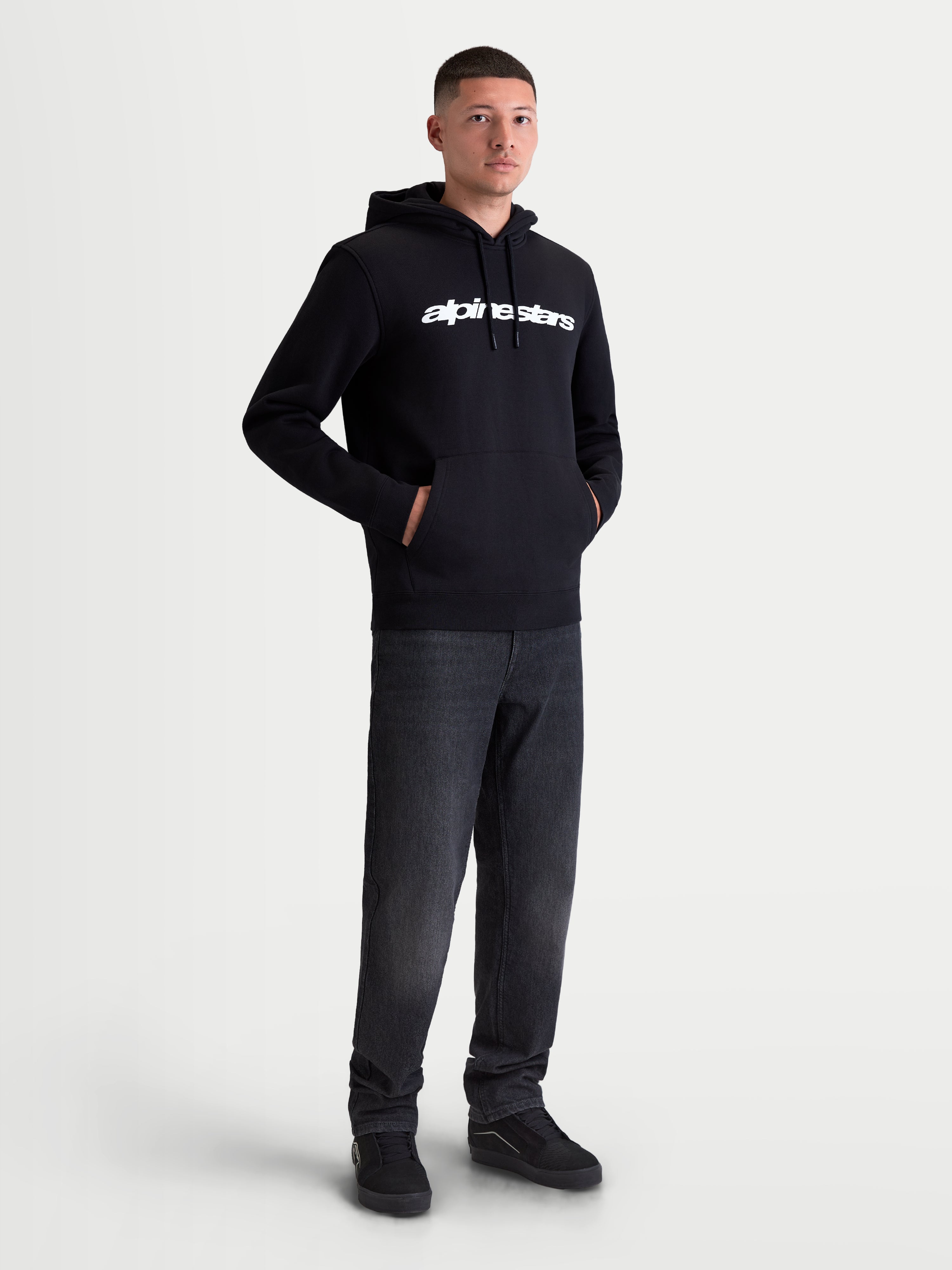 Alpinestars felpa con cappuccio Race Wordmark, felpa in pile sportswear da uomo, nera con logo lineare bianco sul petto, cappuccio con cordini e tasca a marsupio, modello che indossa il prodotto.