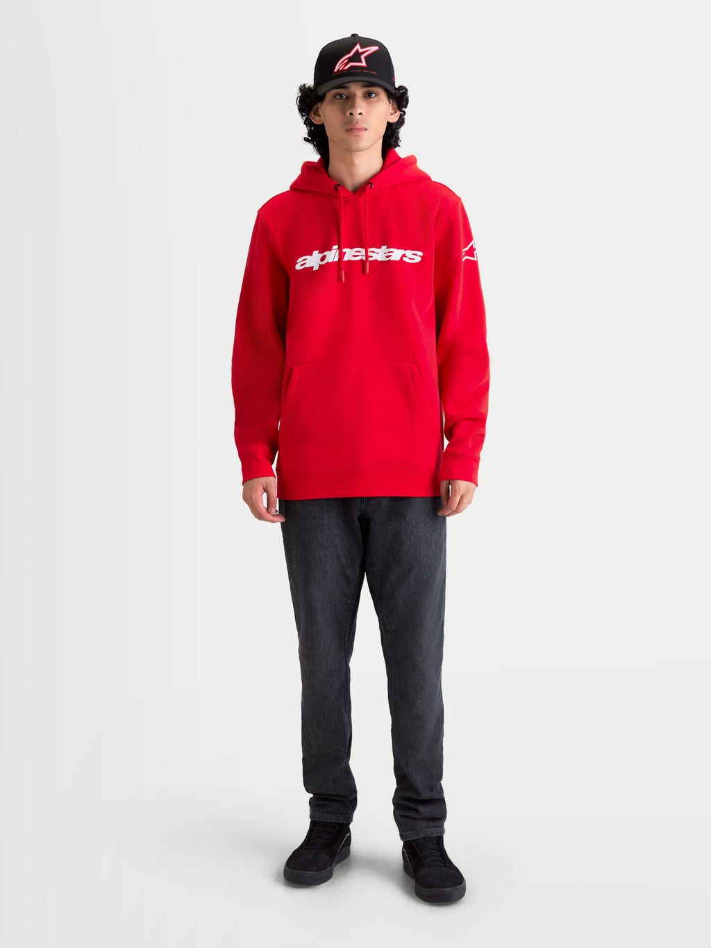 Alpinestars Felpa con cappuccio Race Wordmark, pile sportswear rosso con logo wordmark bianco sul petto e logo sulla manica, tasca a marsupio e cappuccio con cordino, indossata da un modello per un look casual ispirato al motorsport.