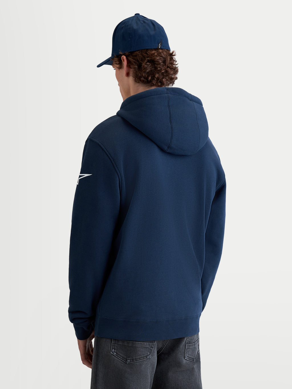 Alpinestars Felpa con cappuccio Race Wordmark, felpa sportswear da uomo in pile, blu navy e bianco, vista posteriore su modello con logo Ageless bianco sulla manica e cappuccio autofoderato.