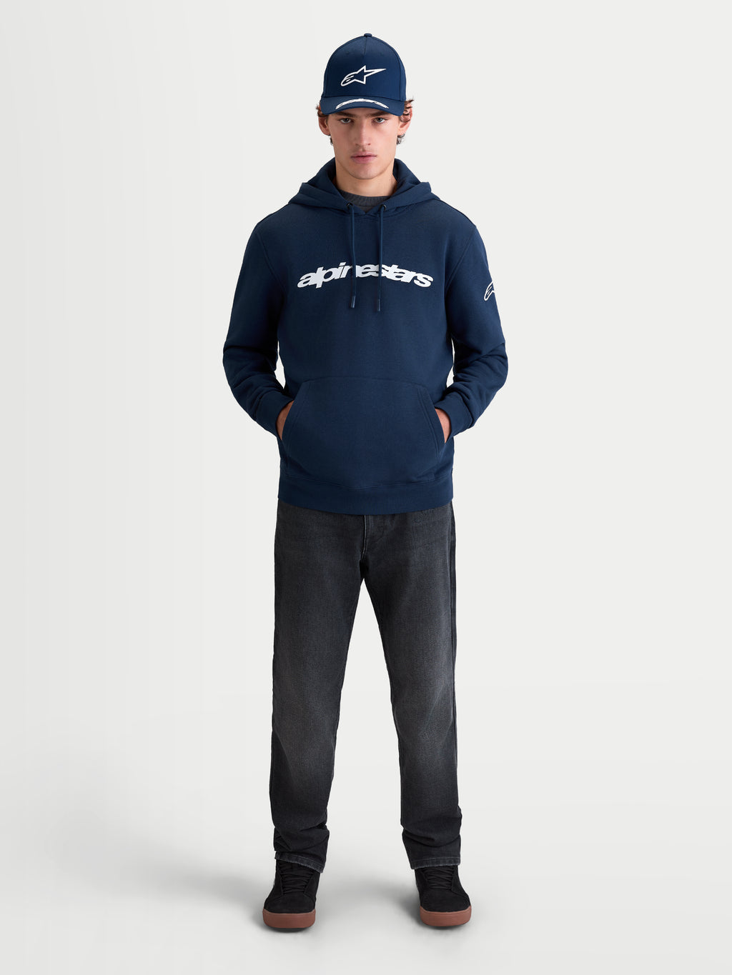 Alpinestars Felpa con cappuccio Race Wordmark, felpa sportswear in pile per uomo e donna, blu navy e bianca, con logo frontale e logo Ageless sulla manica, vista lifestyle su modello per un look casual ispirato al motorsport.