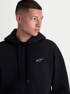 Alpinestars Felpa con cappuccio Pioneer Oversized, felpa sportswear con zip, nera con logo Astars bianco ricamato, cerniera frontale Vislon, cappuccio foderato e vestibilità oversized, indossata da un modello per un look casual quotidiano