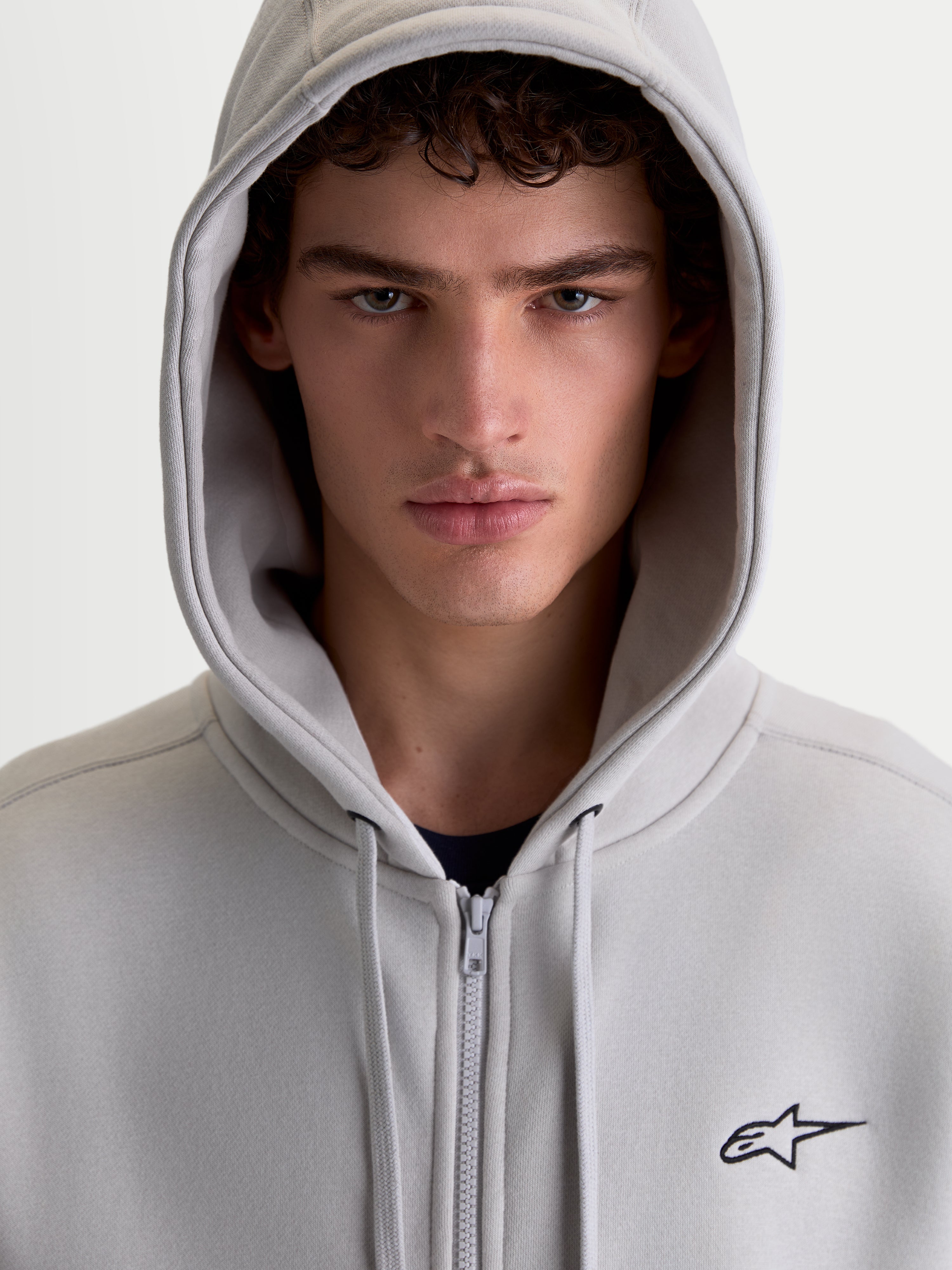 Alpinestars felpa con cappuccio Entity Oversized, felpa sportiva con zip in pile unisex, grigio cemento, logo Astars ricamato e zip Vislon, ritratto in primo piano su modello con cappuccio alzato