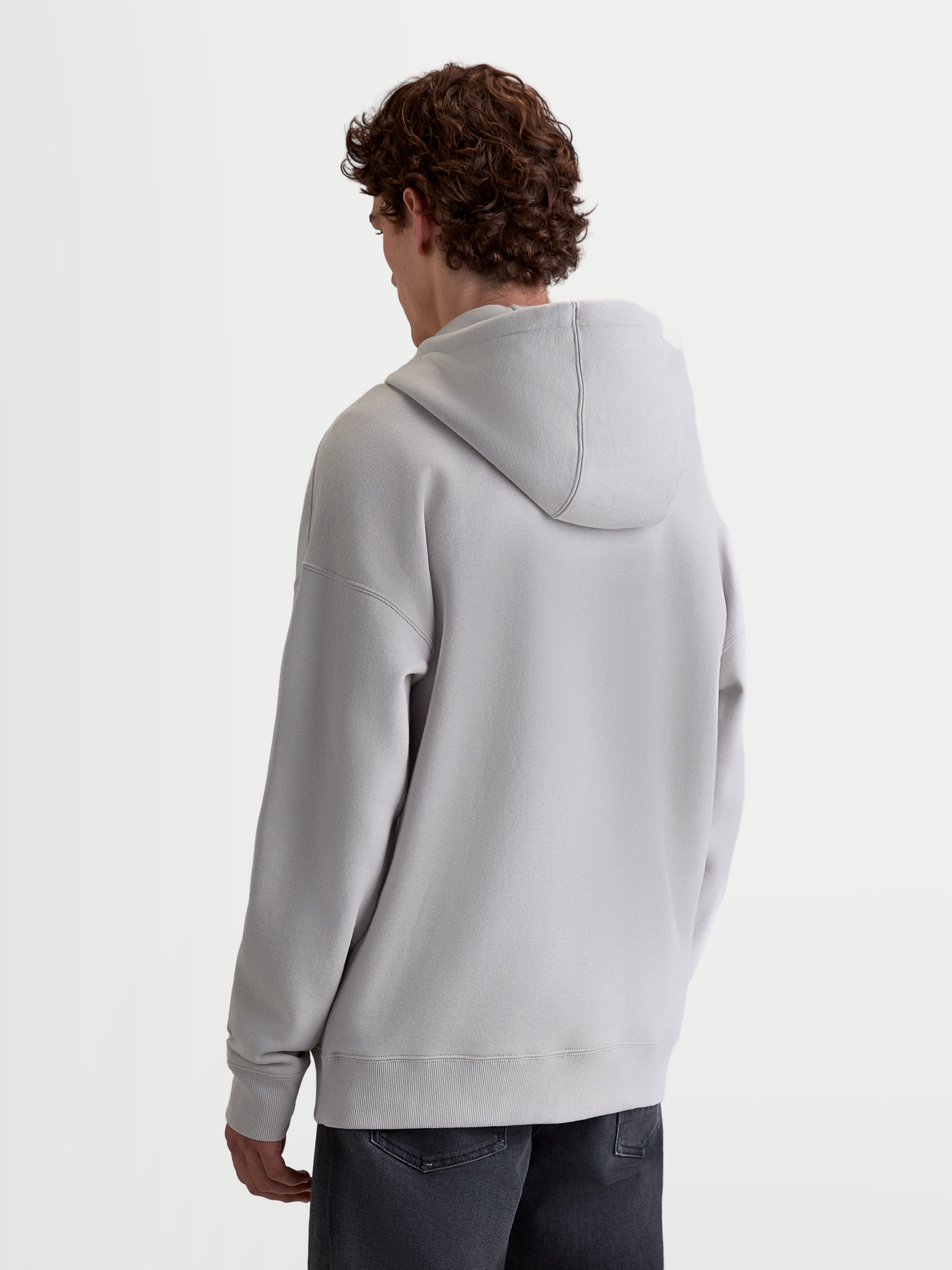 Alpinestars Felpa con cappuccio Entity Oversized, felpa in pile grigio cemento, vista posteriore su modello, vestibilità oversized rilassata con spalle scese, cappuccio autofoderato e bordi a costine, sportswear casual.