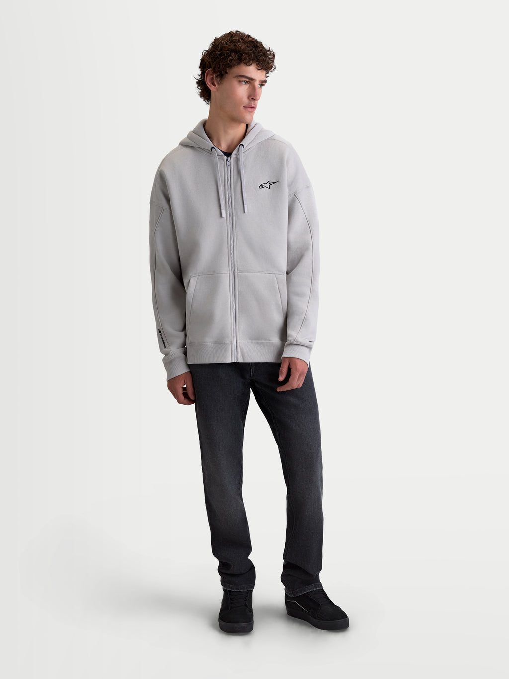 Alpinestars Felpa con cappuccio Entity Oversized, felpa zip intera sportswear unisex, grigio cemento, in misto cotone con vestibilità rilassata, logo Astars ricamato e tasca a marsupio, indossata da un modello per look lifestyle casual.