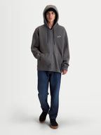 Alpinestars felpa con cappuccio Entity Oversized, felpa premium sportswear in pile con zip, grigio antracite, con zip Vislon frontale, cappuccio con cordini piatti e tasca a marsupio. Vista su modello con silhouette oversized e loghi ricamati sul petto e sulla manica.