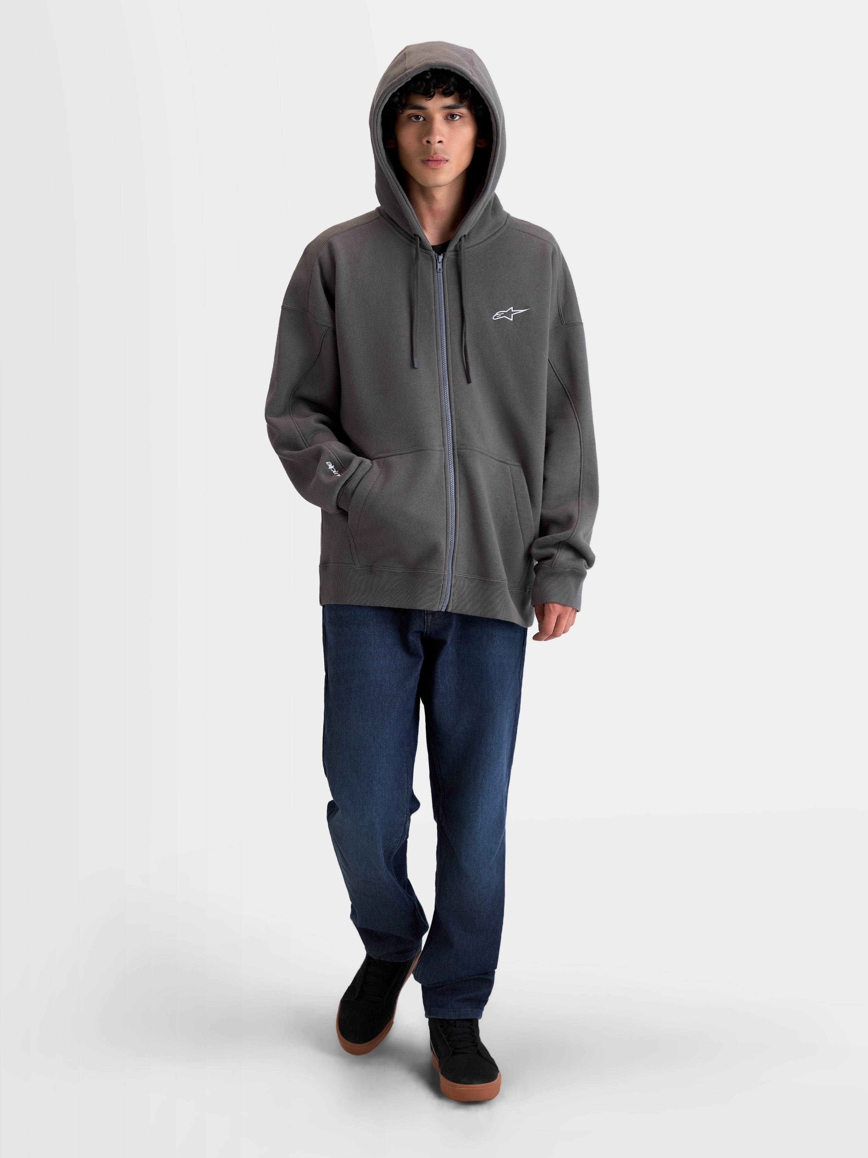 Alpinestars felpa con cappuccio Entity Oversized, felpa premium sportswear in pile con zip, grigio antracite, con zip Vislon frontale, cappuccio con cordini piatti e tasca a marsupio. Vista su modello con silhouette oversized e loghi ricamati sul petto e sulla manica.