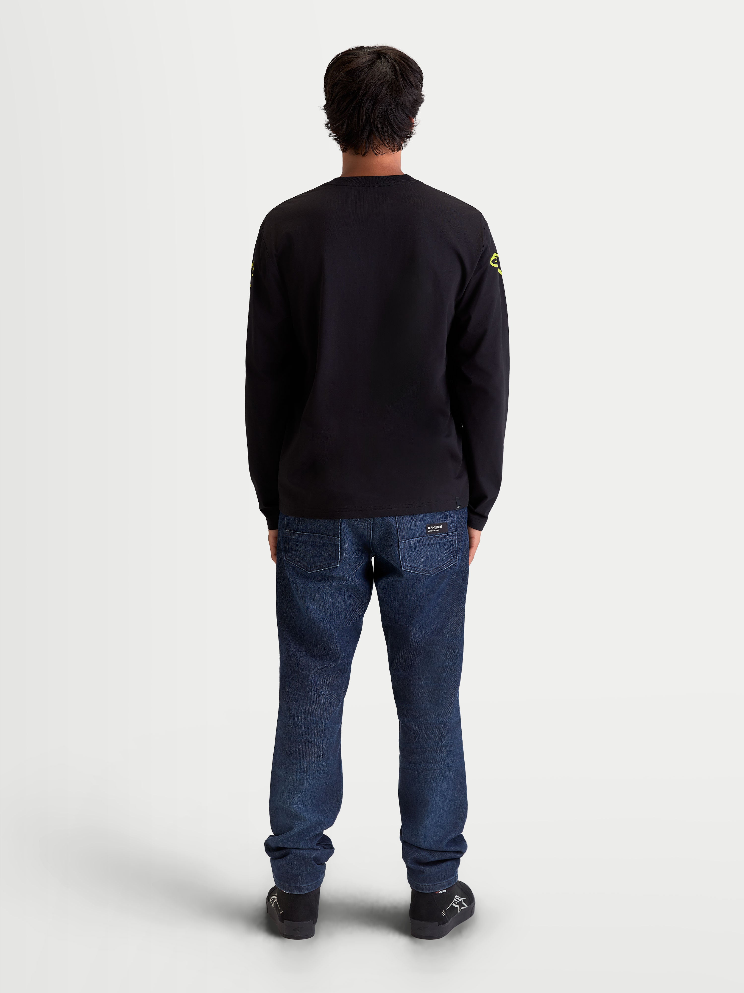 Alpinestars Maglietta Velocifier CSF, maglietta a maniche lunghe sportswear, vista posteriore su modello, nera con loghi gialli sulle spalle, stile casual motorsport, misto cotone e poliestere riciclato, polsini a coste.