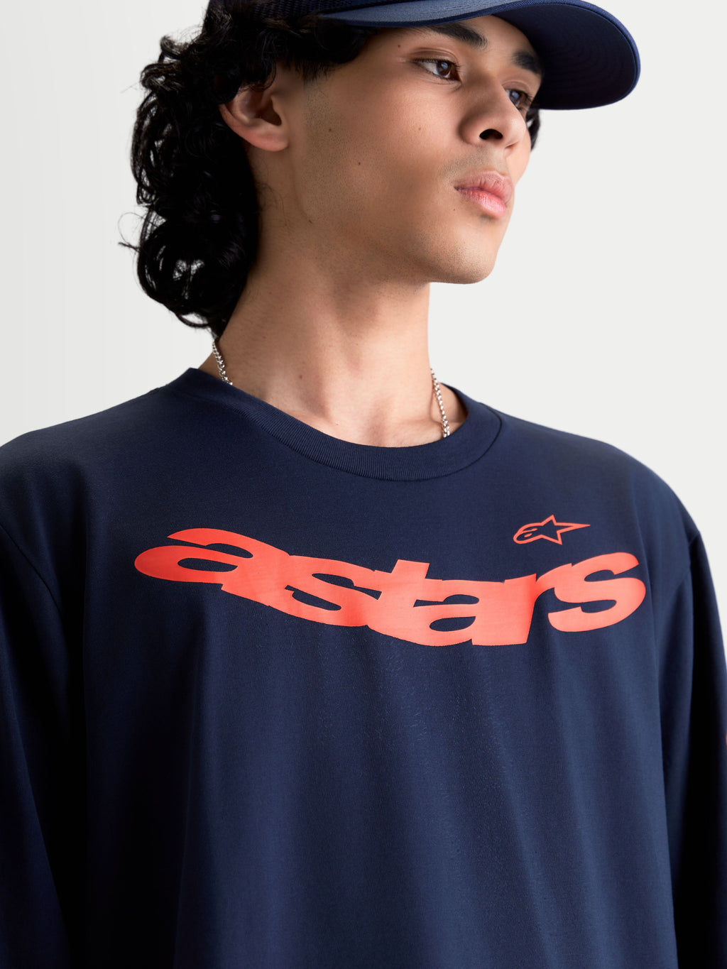 Alpinestars Maglietta Velocifier CSF, maglietta a maniche lunghe, blu navy con grafica Astars curva arancione sul petto, sportswear casual ispirato al motorsport, indossata da un modello