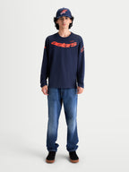 Alpinestars Maglietta Velocifier CSF, maglietta a maniche lunghe da uomo indossata da un modello, blu navy e rosso, con grafica Astars curva sul davanti e loghi sulle spalle, stile casual ispirato al motorsport