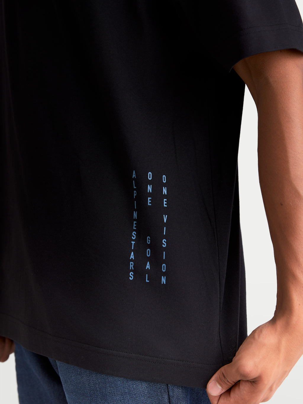 Alpinestars Maglietta Chalk Oversized CSF, maglietta sportswear a maniche corte, nera e blu, con branding verticale One Goal One Vision sul lato, vestibilità oversize rilassata, in misto cotone e poliestere, dettaglio su modello.