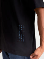 Alpinestars Maglietta Chalk Oversized CSF, maglietta sportswear a maniche corte, nera e blu, con branding verticale One Goal One Vision sul lato, vestibilità oversize rilassata, in misto cotone e poliestere, dettaglio su modello.
