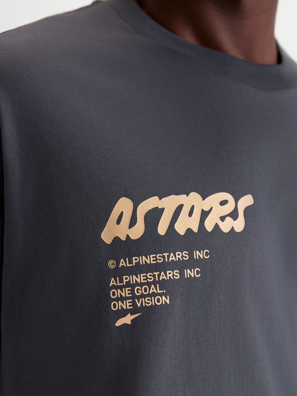 Alpinestars maglietta Chalk Oversized CSF, maglietta a maniche corte grigio antracite e beige, dettaglio ravvicinato del logo Astars e del motto One Goal One Vision sulla parte anteriore, stile casual sportivo lifestyle con vestibilità oversize.