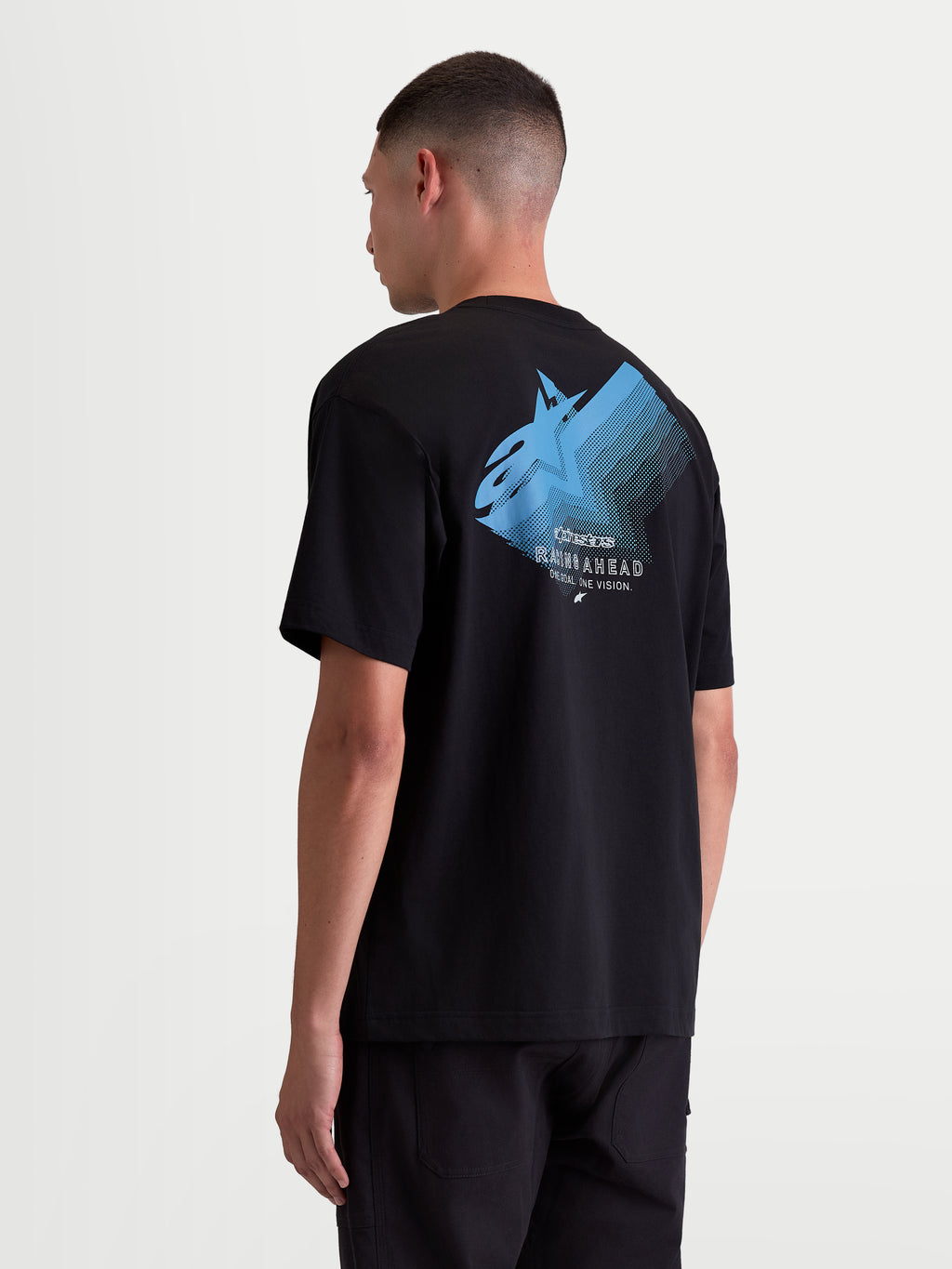 Alpinestars Maglietta Ghost Oversized CSF, maglietta da uomo a maniche corte, nera con grafica blu. Vista posteriore su modello con grande logo Astars sfumato e scritte 'Racing Ahead' e 'One Goal. One Vision.'. Vestibilità oversized rilassata in misto cotone per abbigliamento casual motorsport.