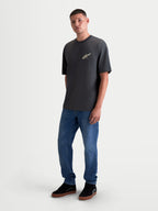 Alpinestars Maglietta Ghost Oversized CSF, maglietta a maniche corte da uomo, grigio antracite, vestibilit  oversize rilassata, logo Astars stampato sul petto, indossata da un modello con jeans blu, stile sportswear