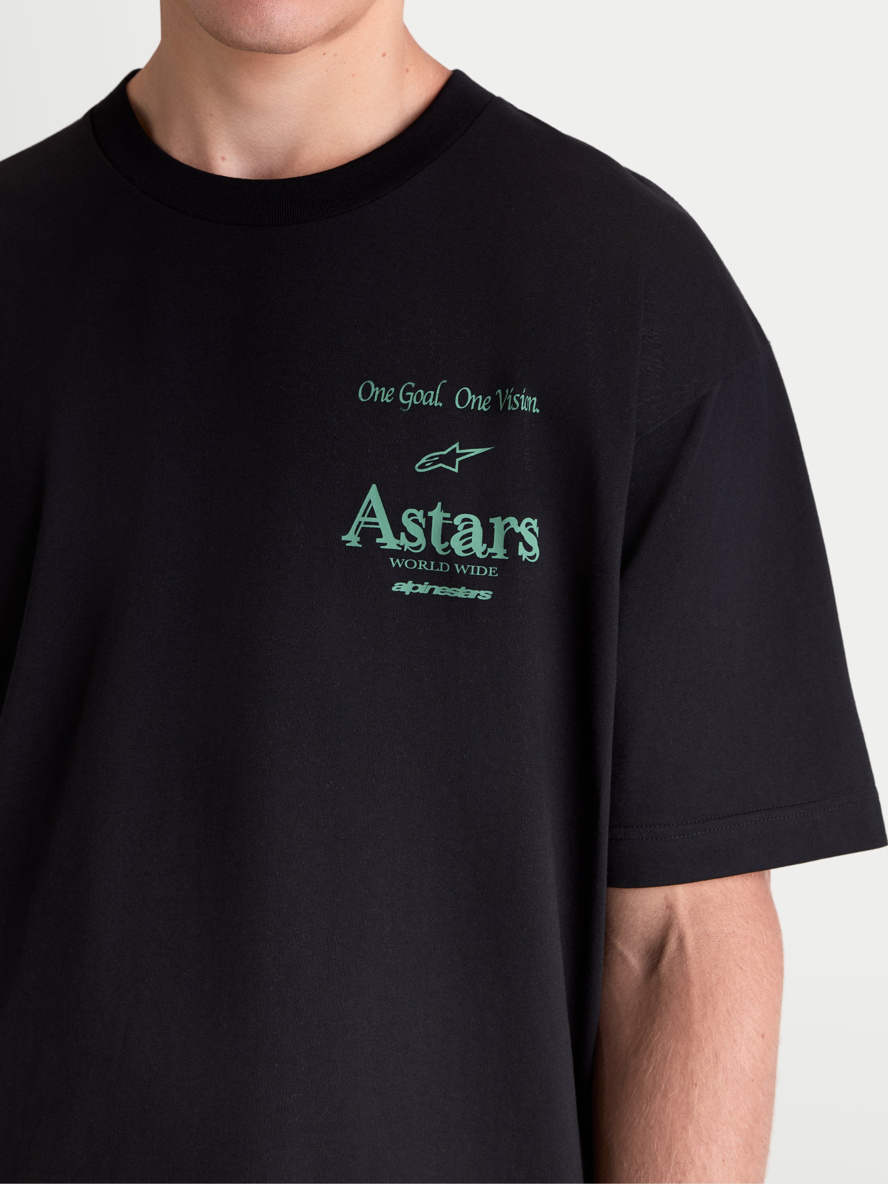 Alpinestars maglietta Post Oversized CSF, maglietta a maniche corte sportswear, nera con grafiche verdi, primo piano su modello che mostra la vestibilità oversized, con scritta 'One Goal. One Vision.' e marchio Astars, realizzata in misto cotone premium