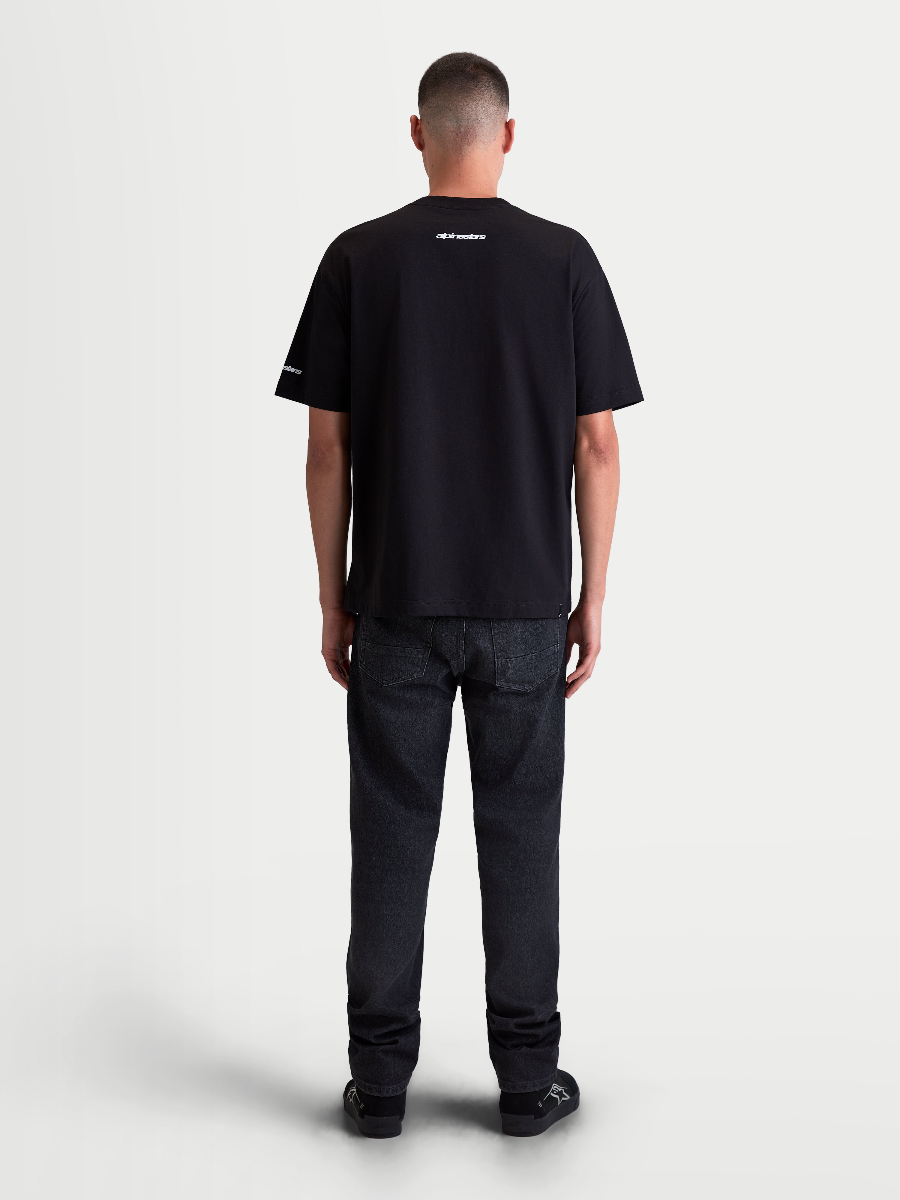 Alpinestars Maglietta Mandate Oversized CSF, maglietta sportswear a maniche corte unisex, nera, in misto cotone e poliestere, vista posteriore su modello con grafiche bianche in puff-print su collo e manica, vestibilità oversized rilassata.