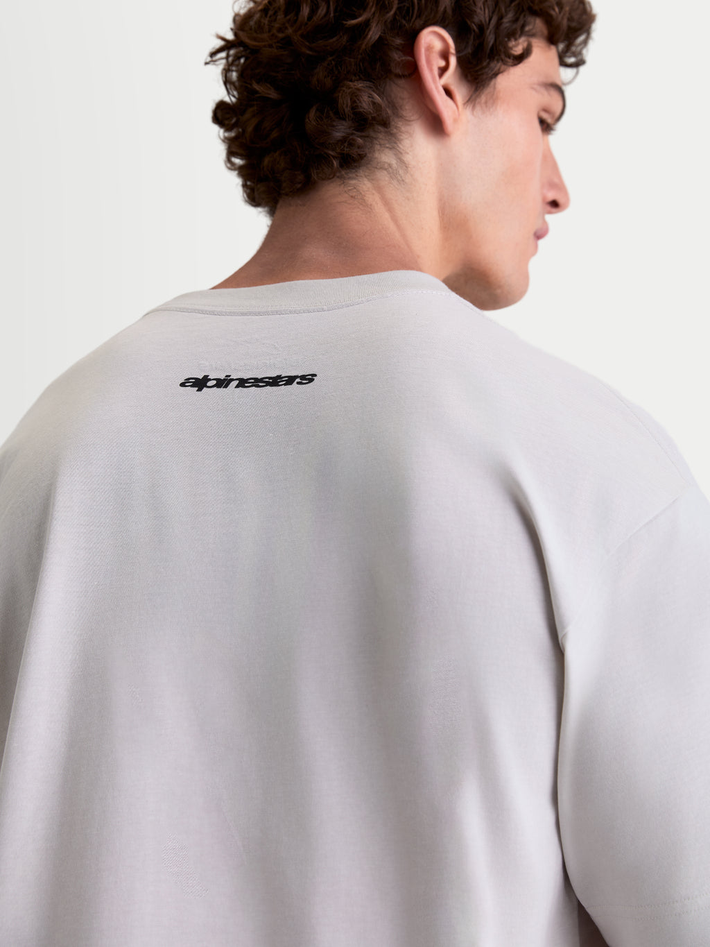 Alpinestars Maglietta Prelude Oversized CSF, maglietta sportswear a maniche corte da uomo, grigio cemento e nero, vista posteriore su modello con logo Alpinestars, vestibilità oversized rilassata in misto cotone e poliestere.