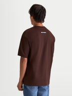 Alpinestars Maglietta Prelude Oversized CSF, maglietta a maniche corte marrone, vista posteriore su modello con logo Alpinestars bianco sulla parte superiore della schiena, vestibilità rilassata oversized, stile sportswear