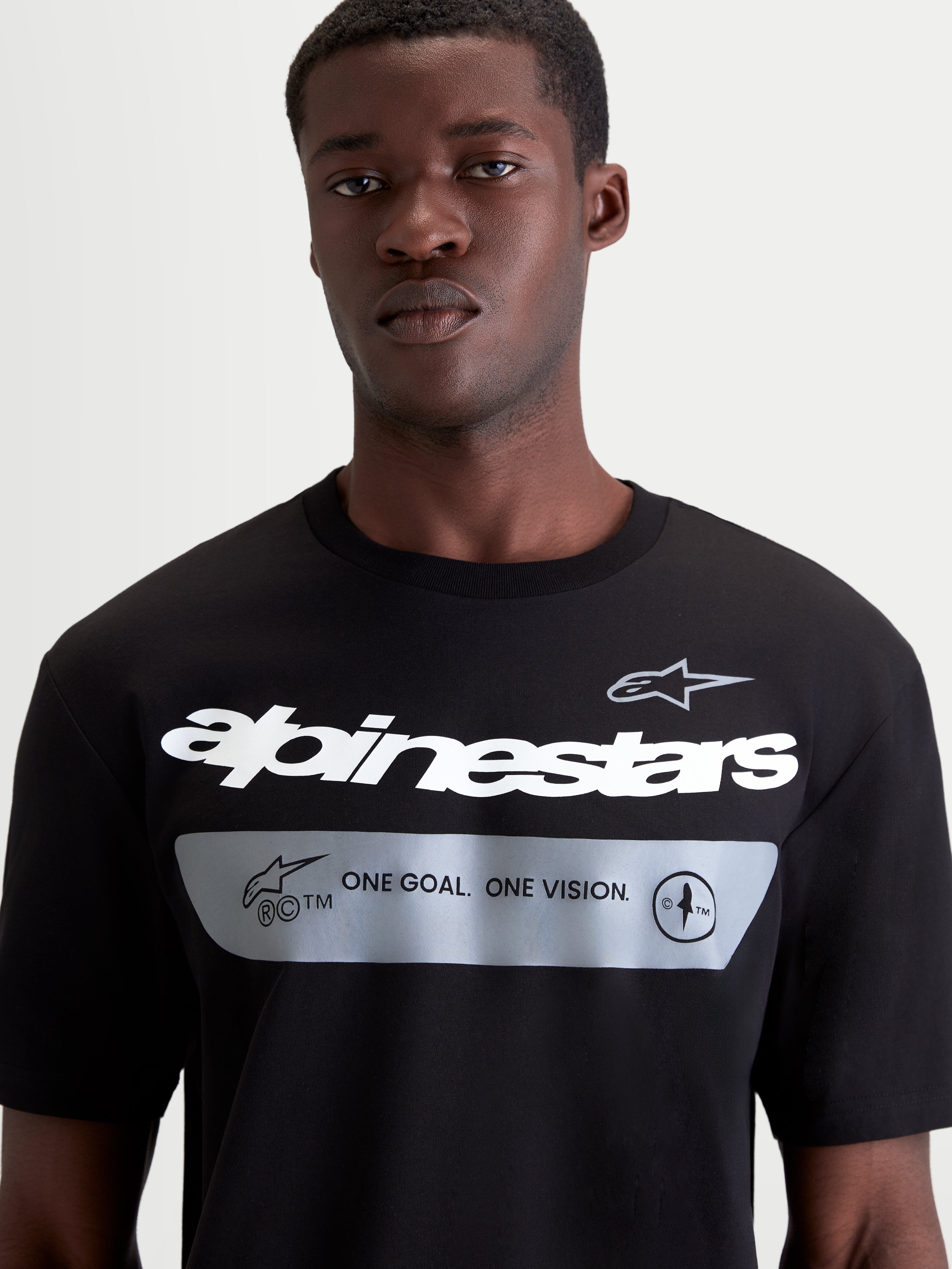 Alpinestars Maglietta Singular CSF, maglietta da uomo a maniche corte, nera con grafica Alpinestars bianca e manifesto del brand "ONE GOAL. ONE VISION." su fondo grigio, stile sportswear casual, primo piano del dettaglio sul petto