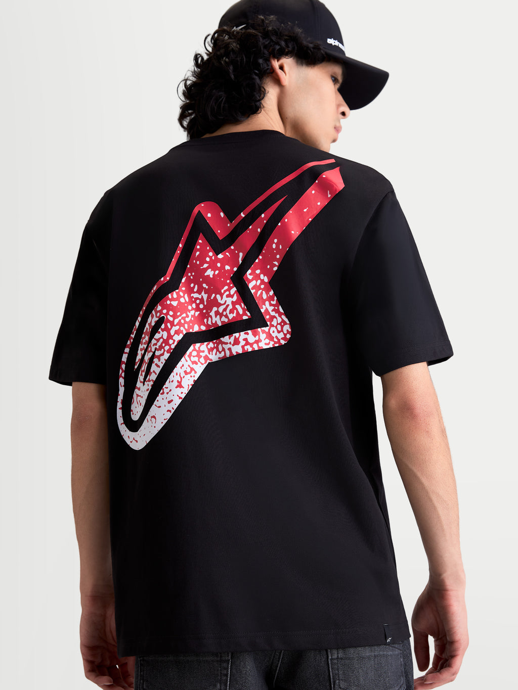 Alpinestars Maglietta Meteor CSF, maglietta a maniche corte nera, vista posteriore su modello con grande logo Astars rosso e bianco sfumato d'ispirazione MX, abbigliamento motorsport casual.