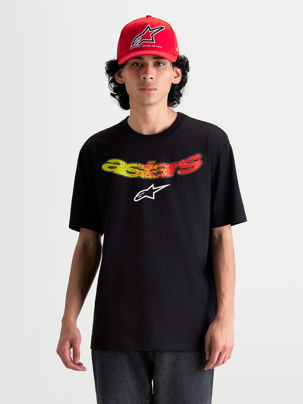 Alpinestars Maglietta Elliptogrit CSF, maglietta a maniche corte da uomo, nera, con scritta Astars curva sfumata rossa e gialla e logo bianco sul petto, stile casual sportswear, indossata da un modello.