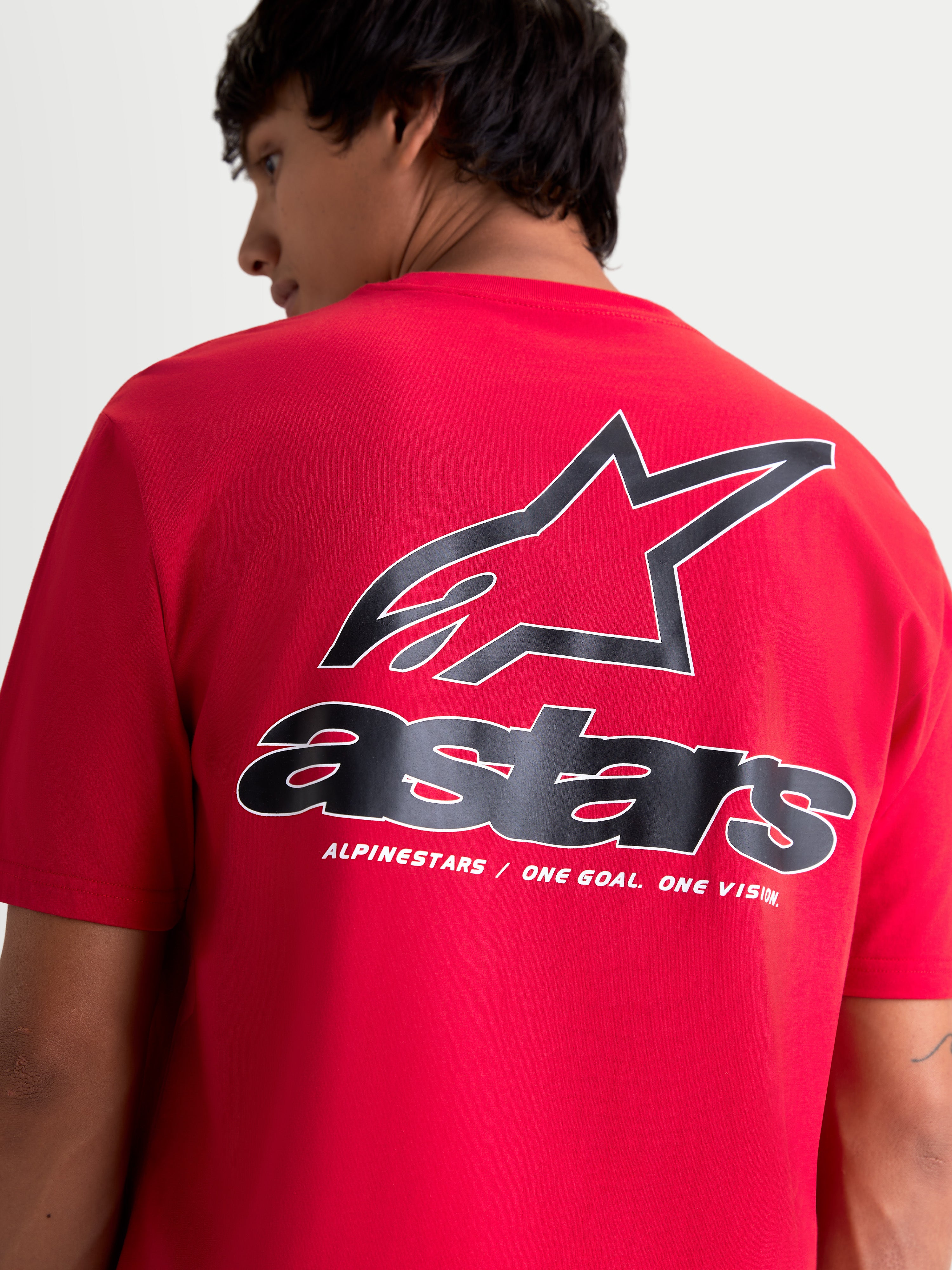 Alpinestars Maglietta Lineout CSF, maglietta a maniche corte rossa, vista posteriore su modello con grande logo Astars nero e bianco e tagline One Goal. One Vision. sulla schiena, stile sportswear casual