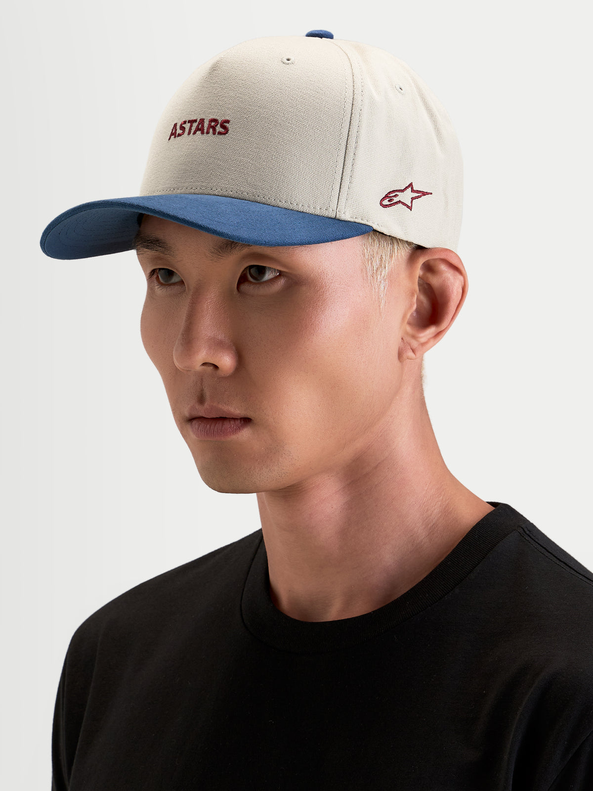 Alpinestars Cappello County Canvas, cappello sportswear in sabbia e blu, indossato da un modello, con visiera curva e logo Astars ricamato