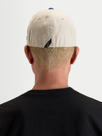 Alpinestars Cappello County Canvas, cappello casual sportswear da uomo, vista posteriore indossato da un modello per mostrare la vestibilità flex-back e il dettaglio del logo sul retro, color sabbia e blu, in tessuto oxford peached