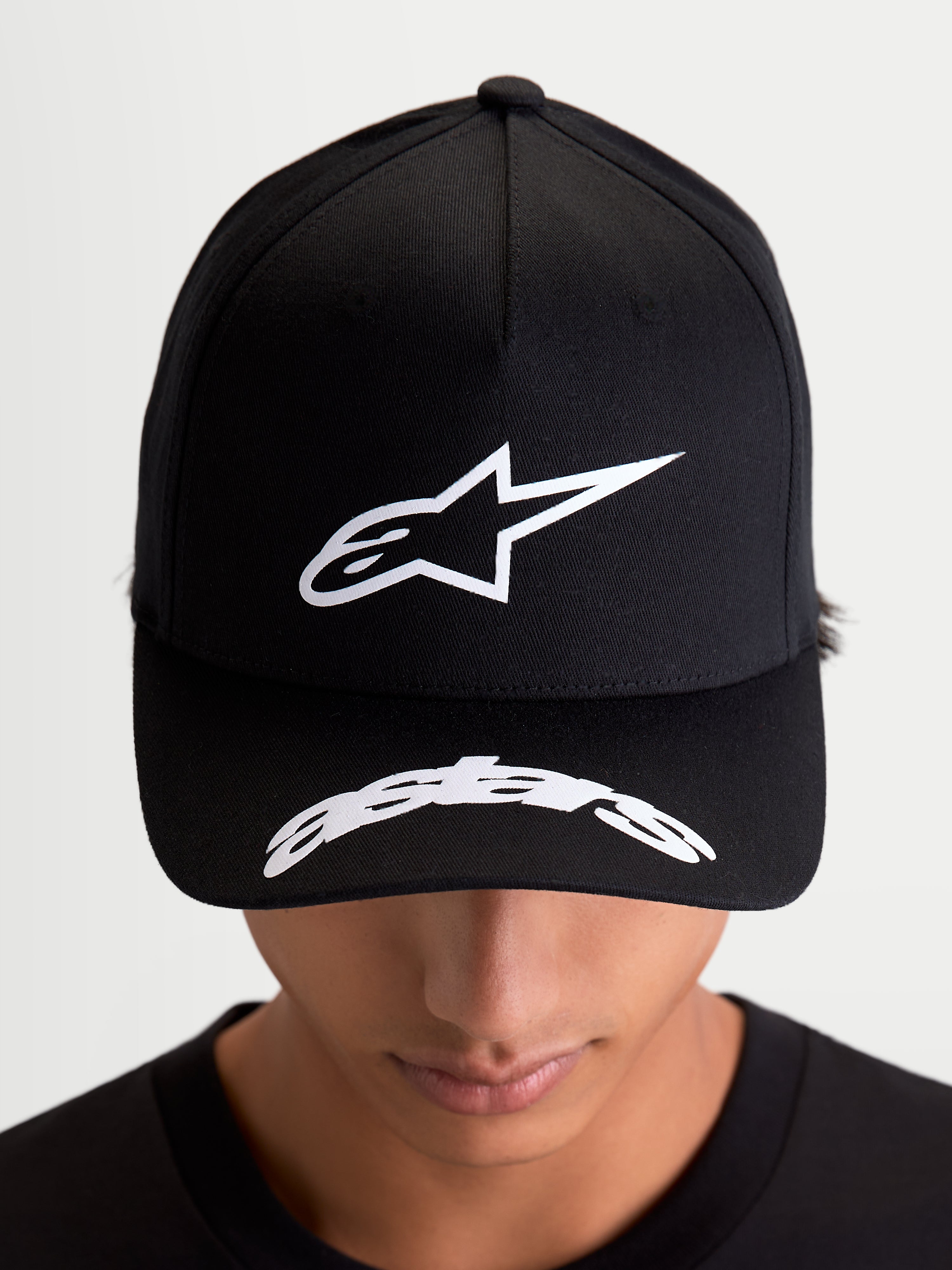 Alpinestars Cappello Arclight, cappello da baseball sportswear, nero e bianco, corona strutturata con logo Astars in puff-print testurizzato e logo curvo sulla visiera, stile motorsport casual, indossato da un modello.