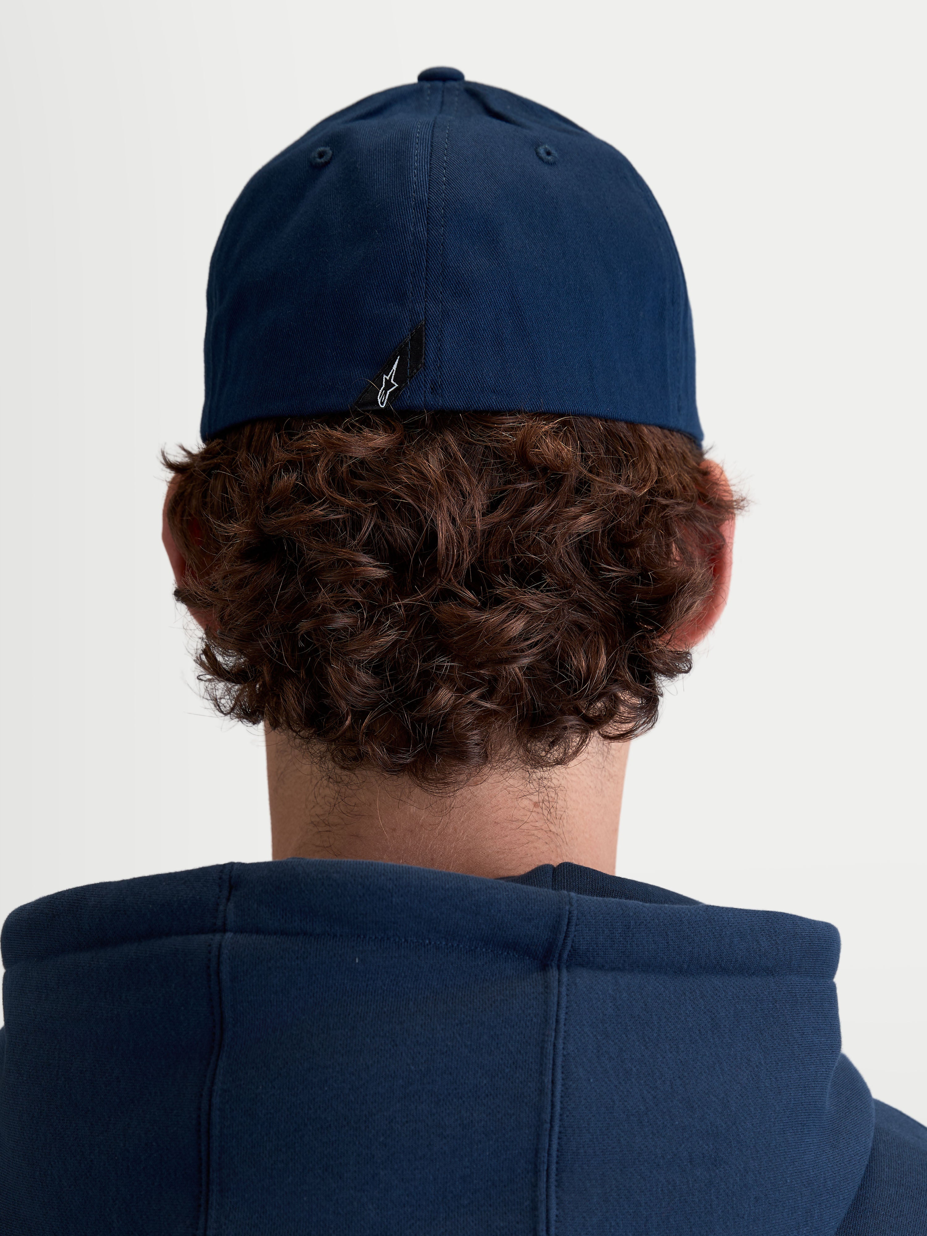 Alpinestars Cappello Arclight, cappello sportswear unisex, blu navy, in resistente twill di cotone con retro flessibile, vista posteriore su modello che mostra il dettaglio dell'etichetta con logo Astars