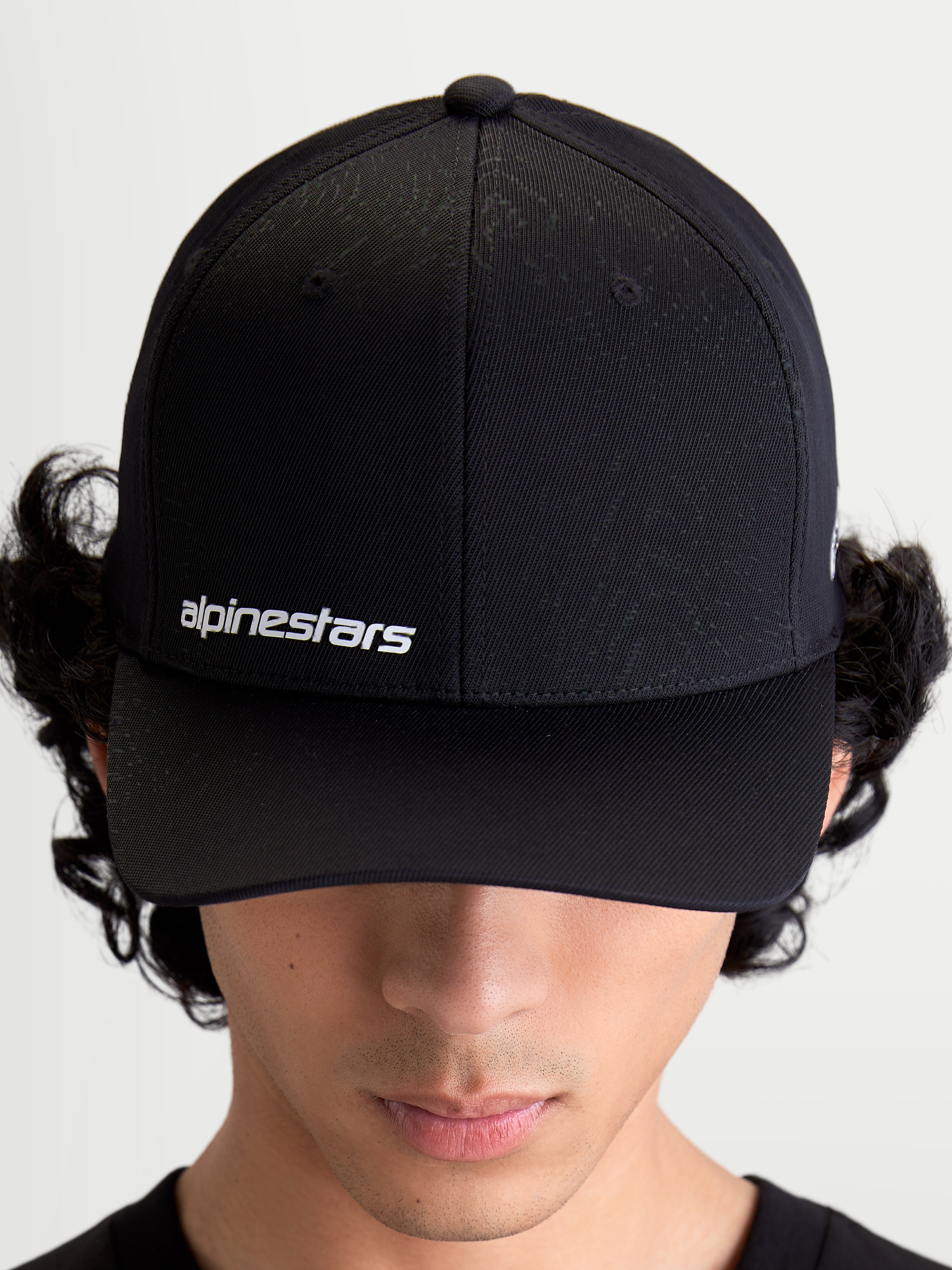 Alpinestars Cappello Points, cappello sportswear nero con visiera curva indossato da un modello, logo testuale Alpinestars bianco sul davanti, realizzato in leggero nylon tactel