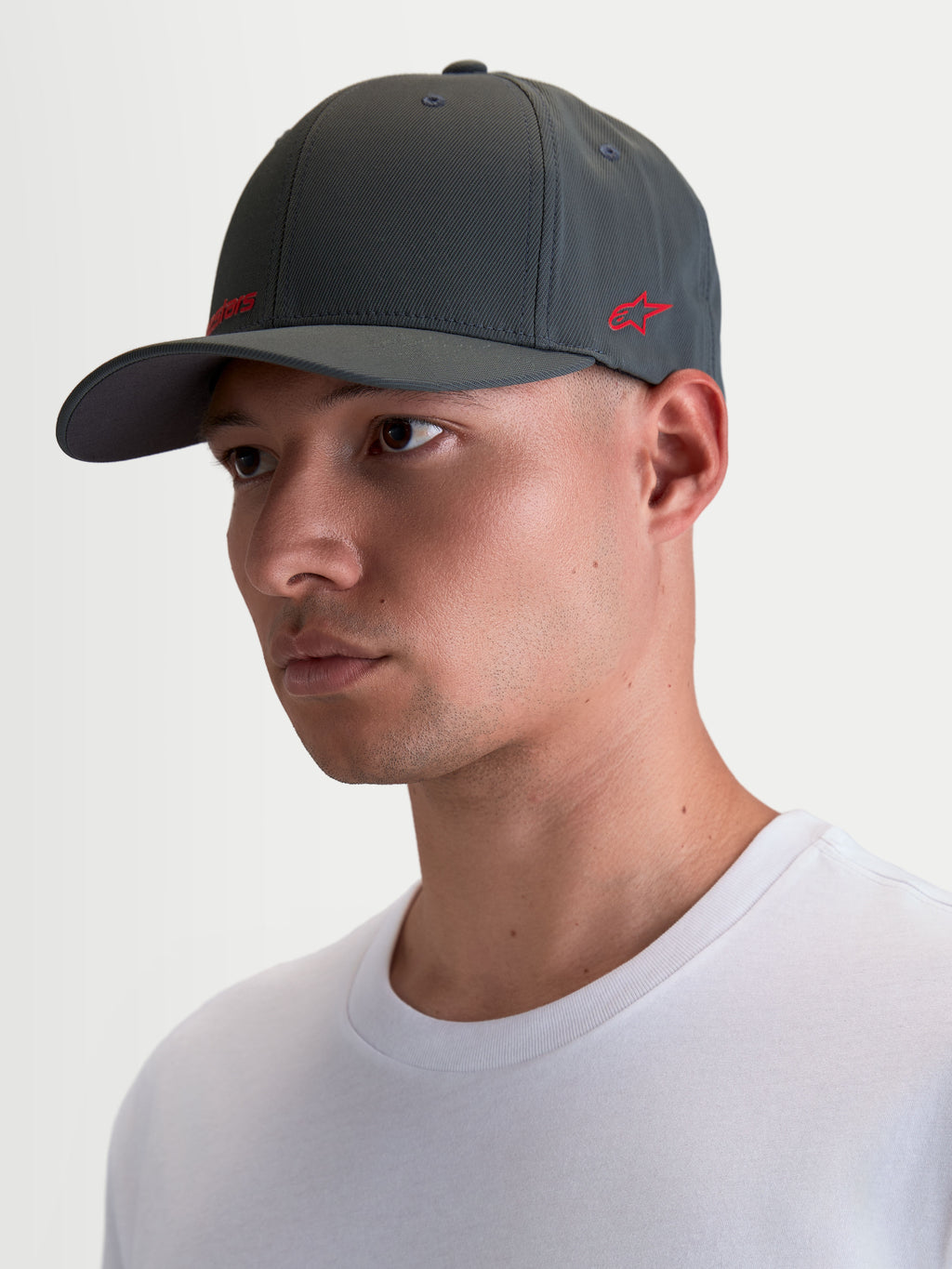 Alpinestars Cappello Points, cappello sportswear con visiera curva indossato da un modello, grigio scuro con logo rosso, in nylon tactel leggero, vestibilità flex-back per il massimo comfort quotidiano