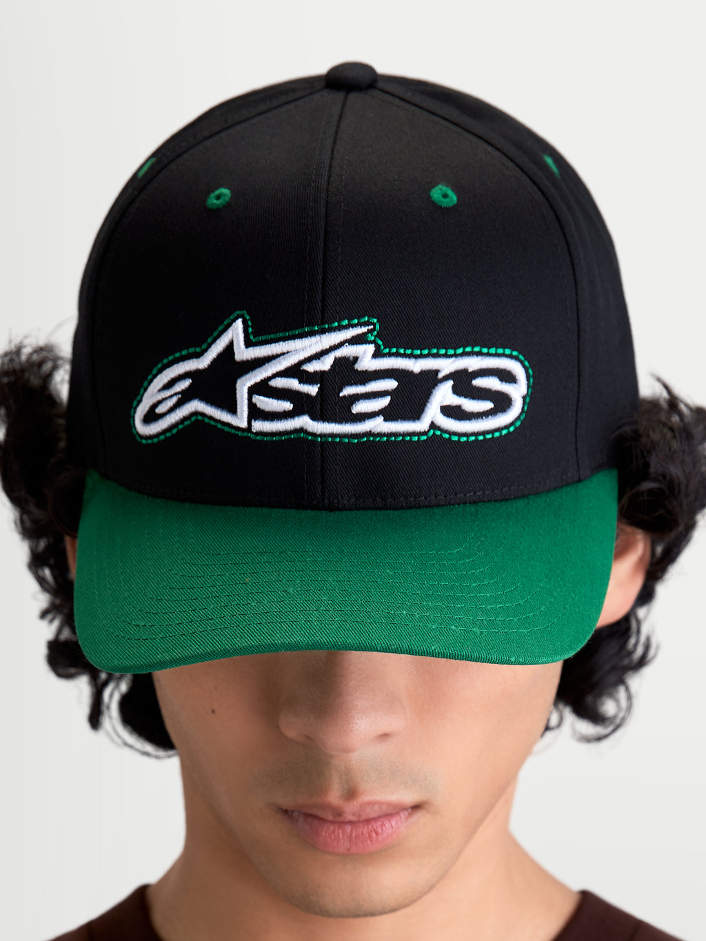 Alpinestars Cappello Retro Snapback, cappello snapback stile sportswear ispirato al motorsport, unisex, nero e verde, in twill di cotone, vista frontale su modello con logo Astars e dettaglio cucitura verde a contrasto.