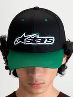 Alpinestars Cappello Retro Snapback, cappello snapback stile sportswear ispirato al motorsport, unisex, nero e verde, in twill di cotone, vista frontale su modello con logo Astars e dettaglio cucitura verde a contrasto.