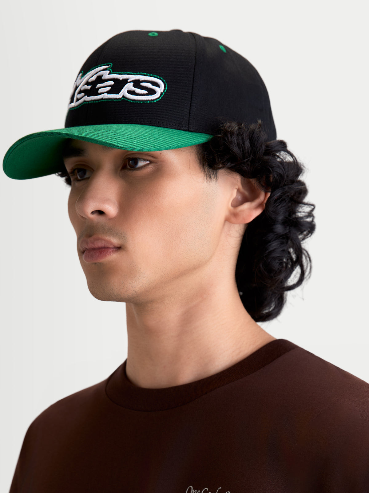 Alpinestars Cappello Retro Snapback, cappello sportswear casual indossato da un modello, nero e verde, con visiera curva, corona strutturata e logo Astars ricamato con cucitura verde, twill di cotone.