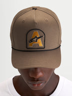 Alpinestars Cappello Acme Snapback, cappello visiera curva da sportswear quotidiano, marrone noce con patch ricamata del logo Astars sul davanti e rifinitura in corda nera, indossato da un modello
