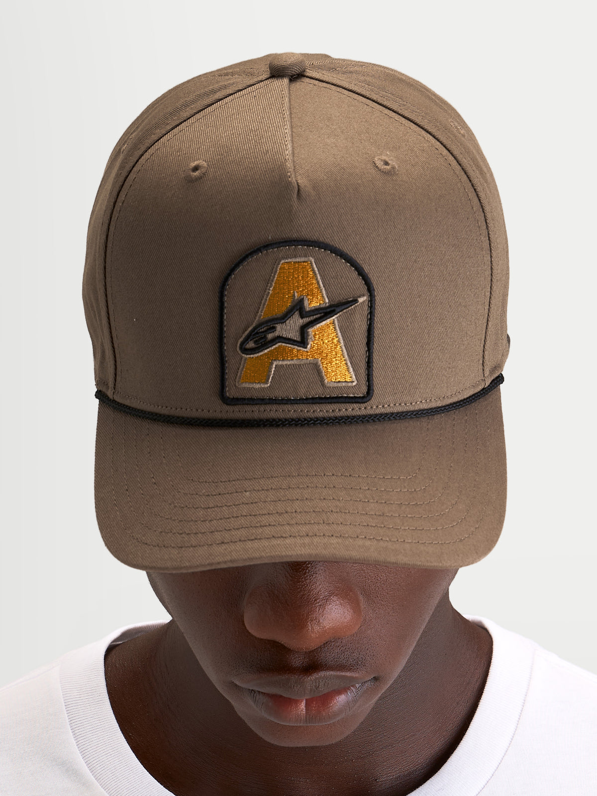 Alpinestars Cappello Acme Snapback, cappello visiera curva da sportswear quotidiano, marrone noce con patch ricamata del logo Astars sul davanti e rifinitura in corda nera, indossato da un modello